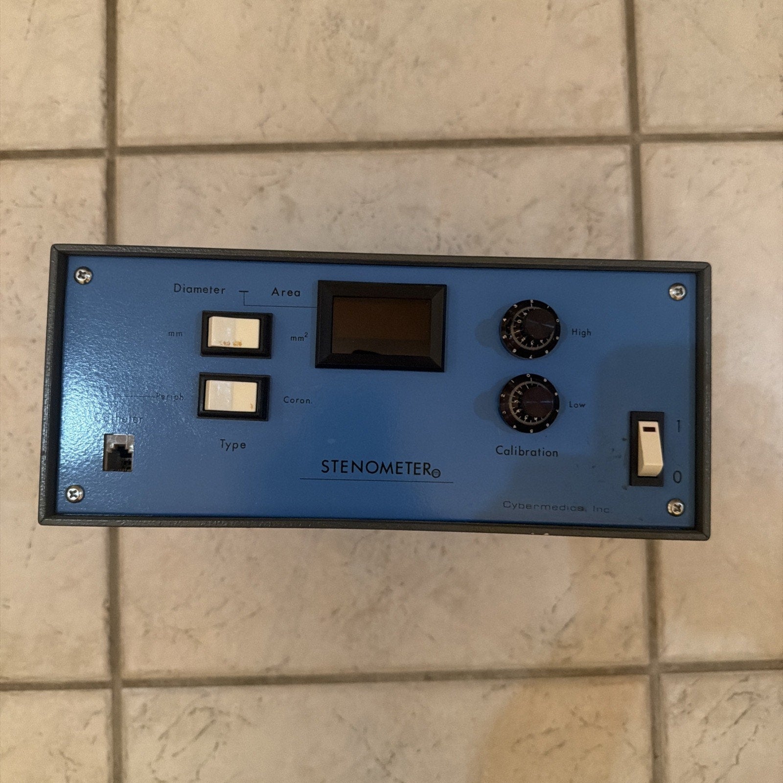 Cybermedics Stenometer cardiology lab instrument with blue front panel, switches, knobs, and digital display on tiled floor