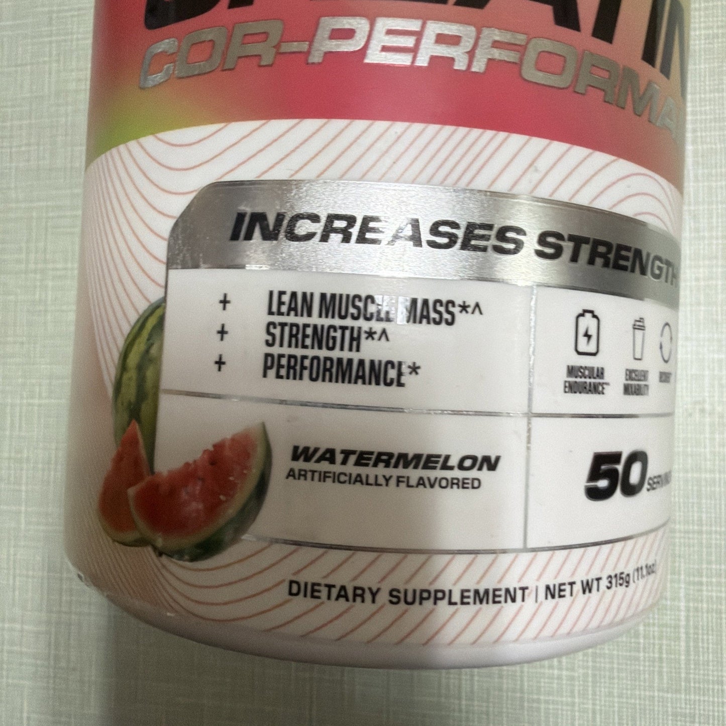 Close-up of a watermelon-flavored dietary supplement label promoting increased lean muscle mass, strength, and performance with icons for muscular endurance and recovery.