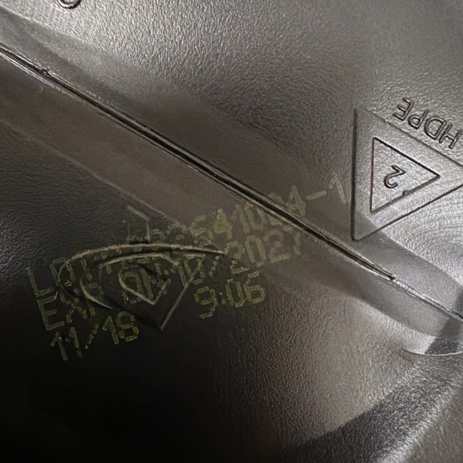 Close-up of a black plastic surface showing yellow printed lot number, expiration date 11/18/2024, time code 9:06, and an embossed recycling symbol with the code "2" and "HDPE" text.