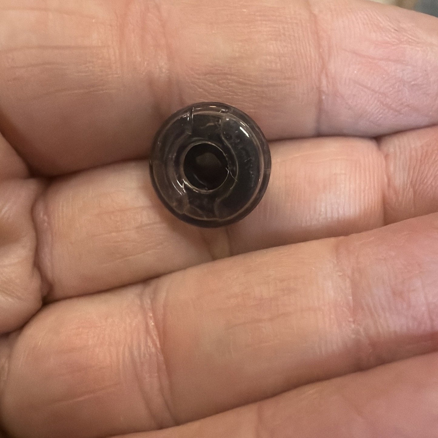 Close-up of a small, translucent black plastic bead with a central hole resting on the fingertips of a hand.