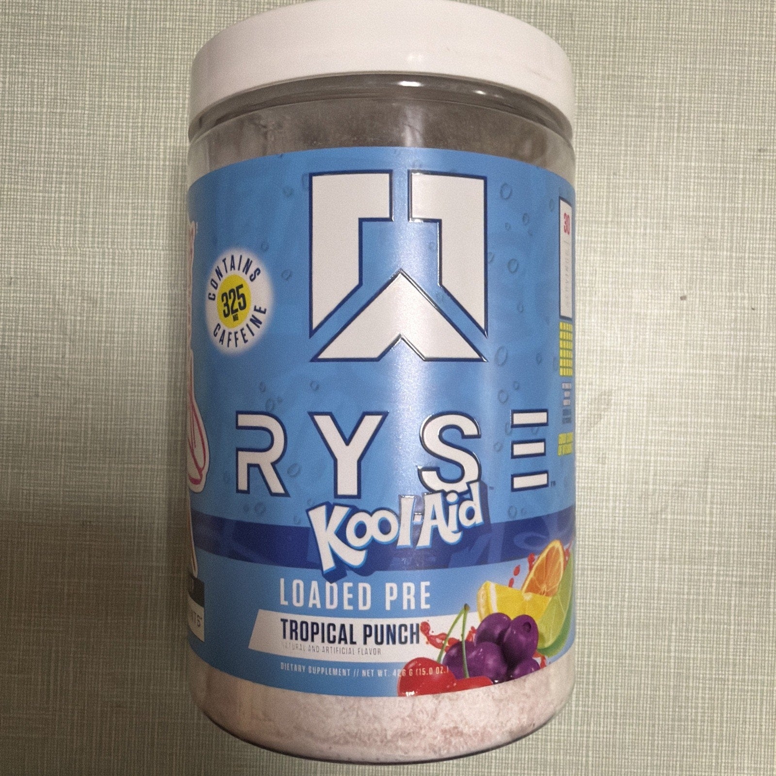 Container of RYSE Kool-Aid Loaded Pre workout supplement in Tropical Punch flavor with a blue label, featuring a large logo, fruit illustrations, and a note about 325 mg caffeine content.