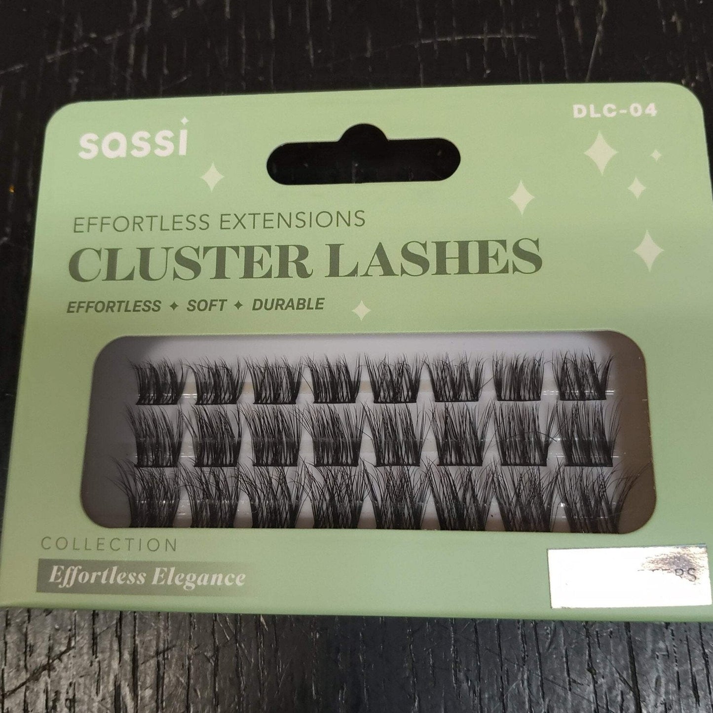 Light green packaging of sassi brand cluster eyelash extensions labeled as effortless, soft, and durable, displaying several rows of black lash clusters through a transparent window.