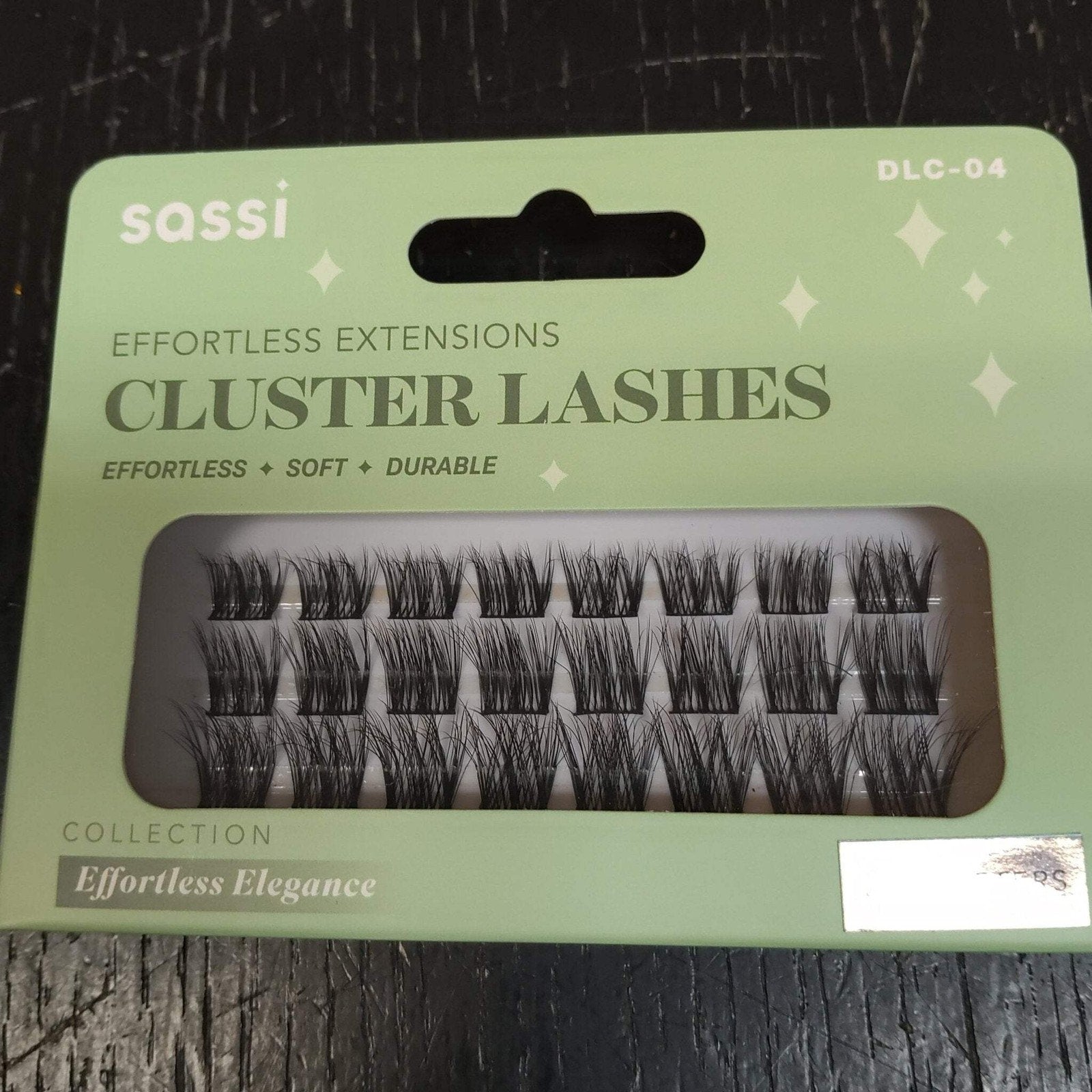 Light green packaging of sassi brand cluster eyelash extensions labeled as effortless, soft, and durable, displaying several rows of black lash clusters through a transparent window.