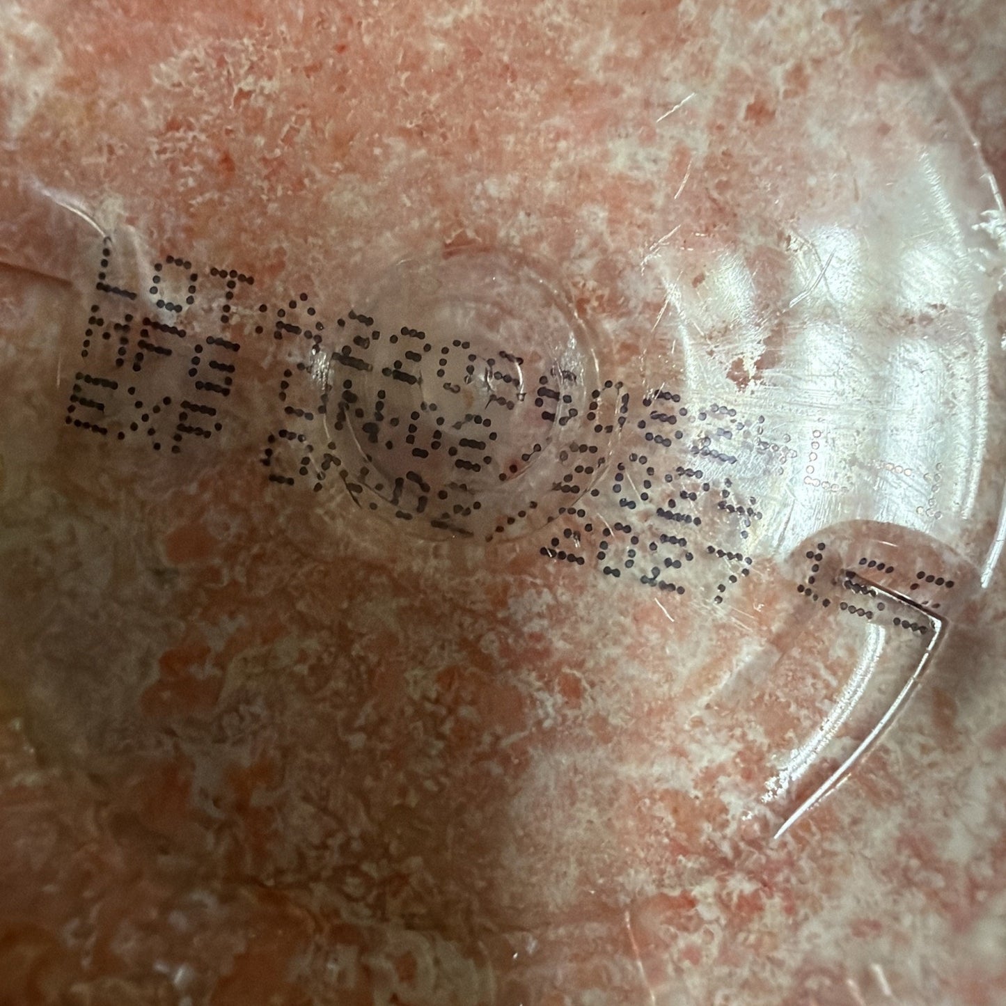 Close-up of a printed lot number, manufacture date of June 2023, and expiration date of April 2027 on a pink marbled plastic surface.