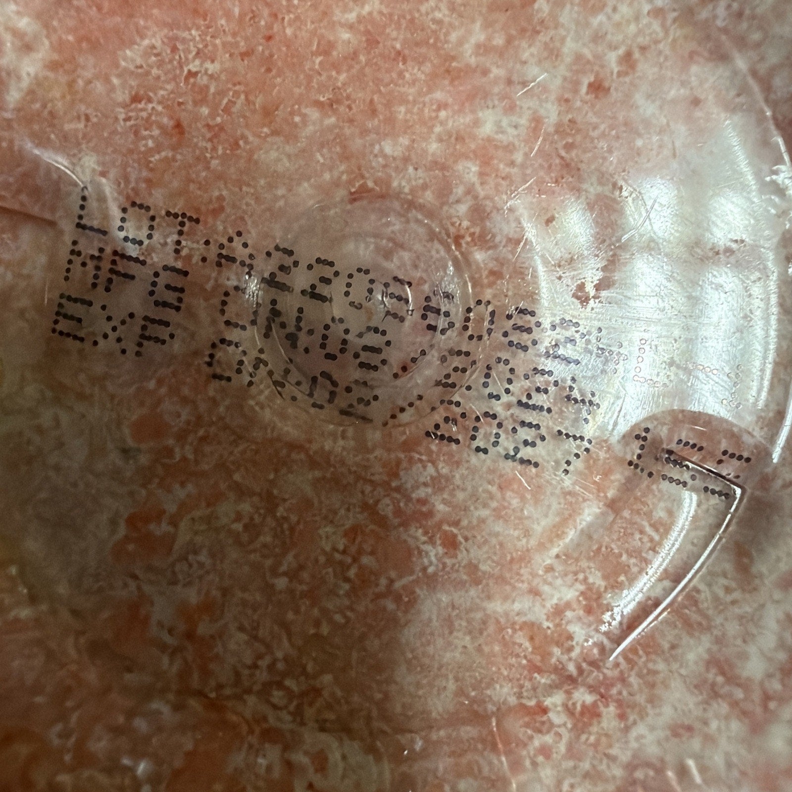 Close-up of a printed lot number, manufacture date of June 2023, and expiration date of April 2027 on a pink marbled plastic surface.