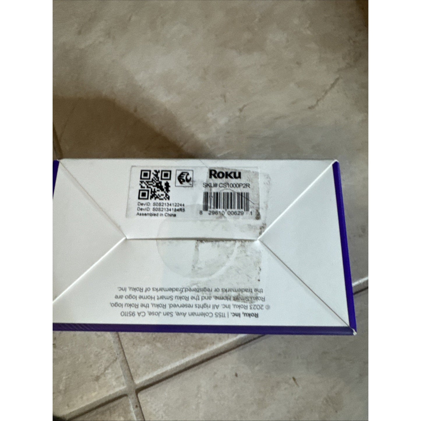 Roku Indoor Camera SE wired 2 pack box label showing barcode and product details on tiled floor background
