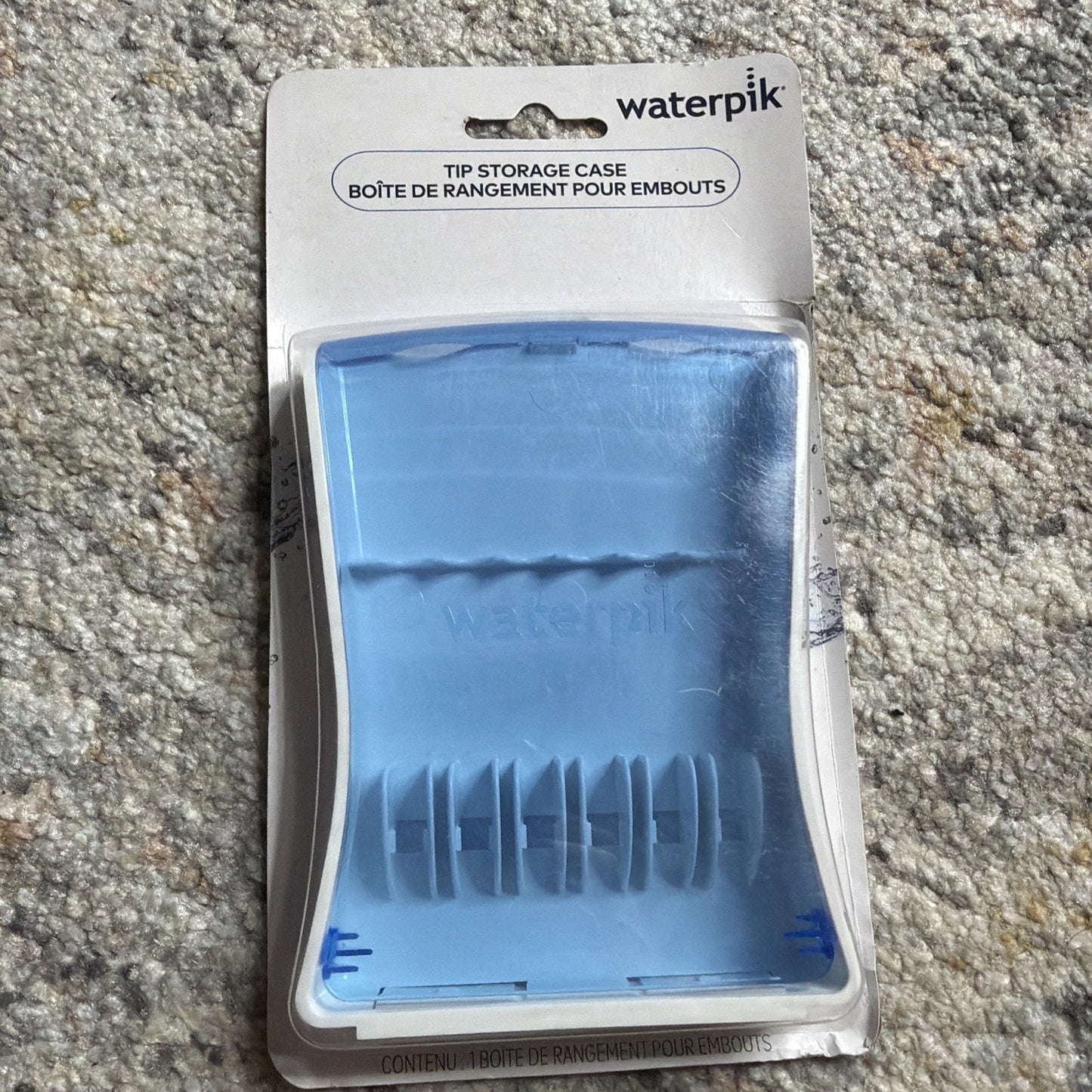 Blue translucent plastic Waterpik tip storage case in original packaging, designed to organize and store multiple replacement tips for Waterpik oral irrigators.