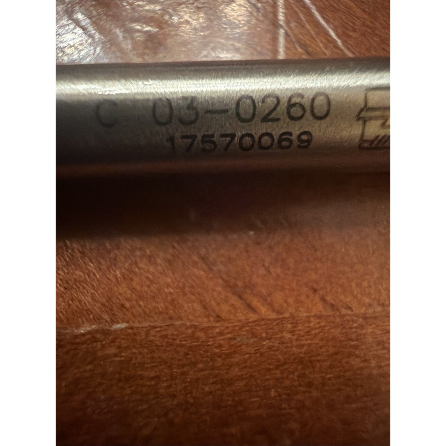 Close-up of a metal tool shaft engraved with the code "C 03-0260" and the number "17570069," resting on a textured wooden surface.