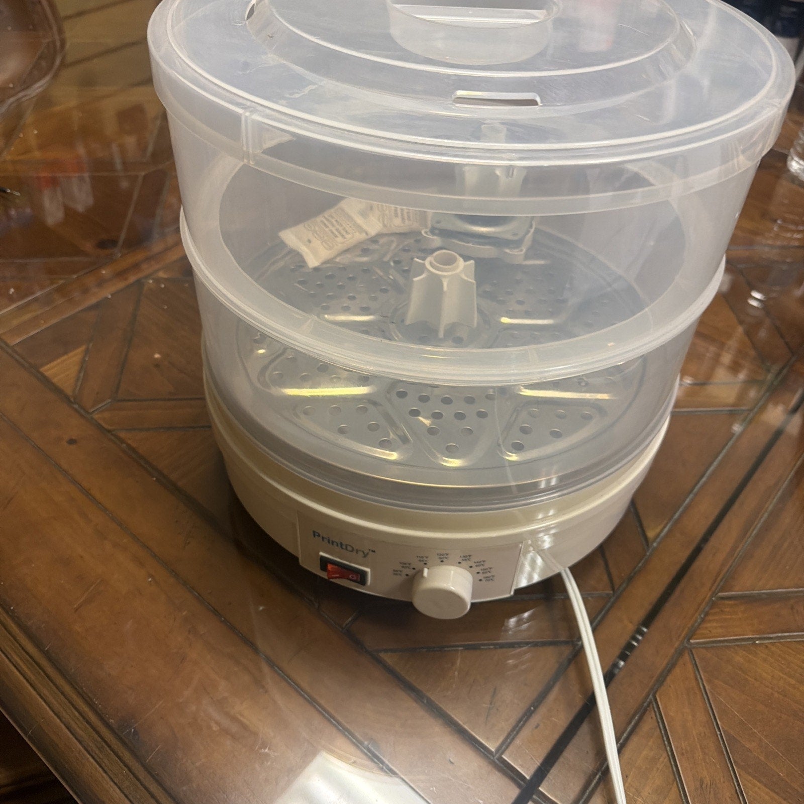 Electric food steamer with transparent plastic tiered containers and a white base featuring a rotary control knob and power switch, placed on a wooden surface.