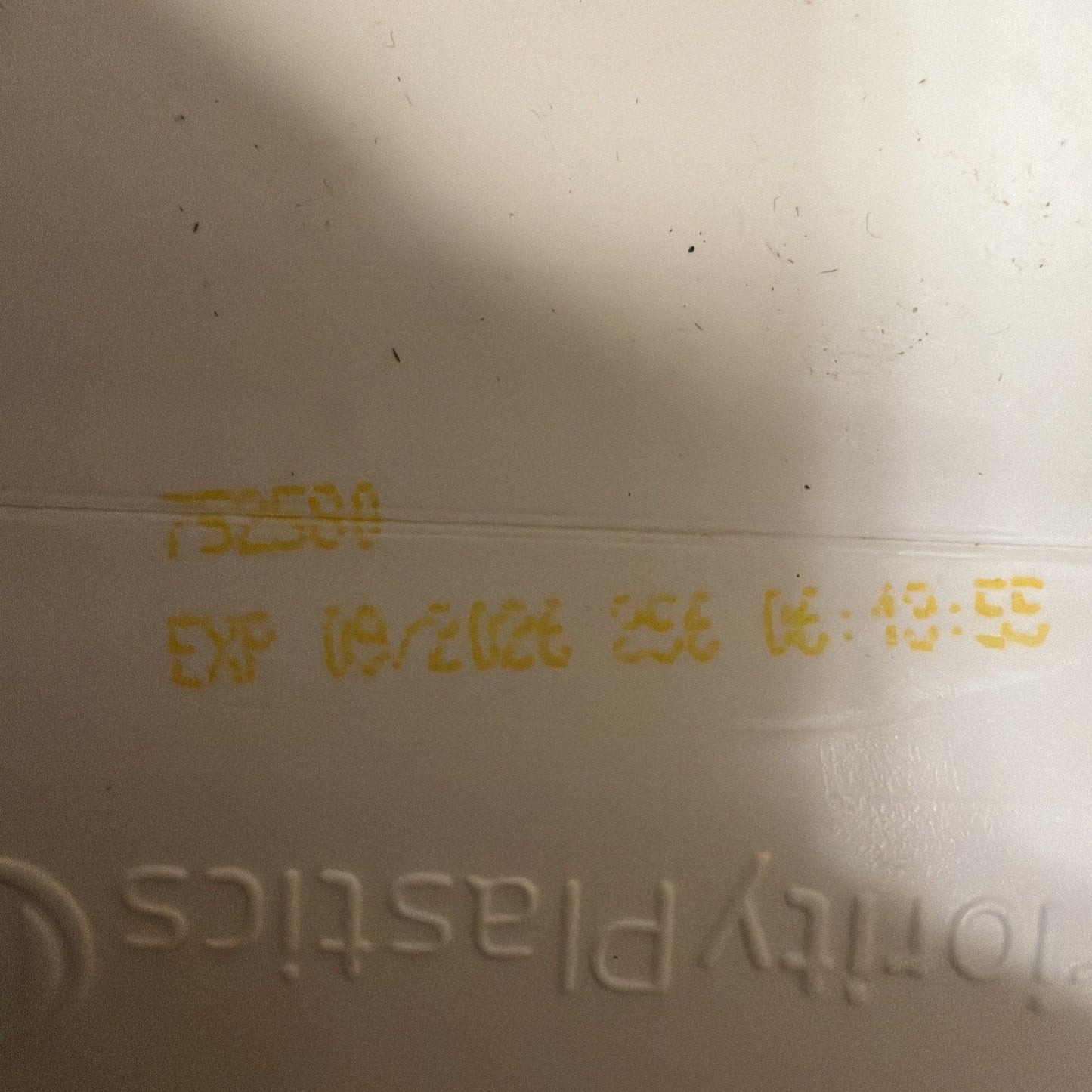 Close-up of yellow printed expiration date 10/2026 and time 06:19:55 on a white plastic surface with partial embossed text showing "tomity plastics.