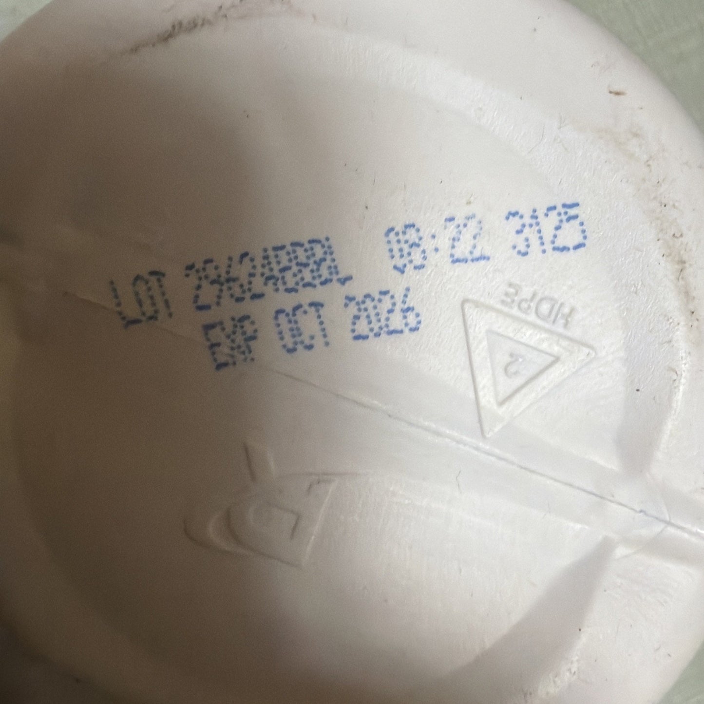 Plastic container bottom showing a blue ink stamp with lot number, manufacturing date, expiration date of October 2026, and a recycling symbol indicating HDPE material.