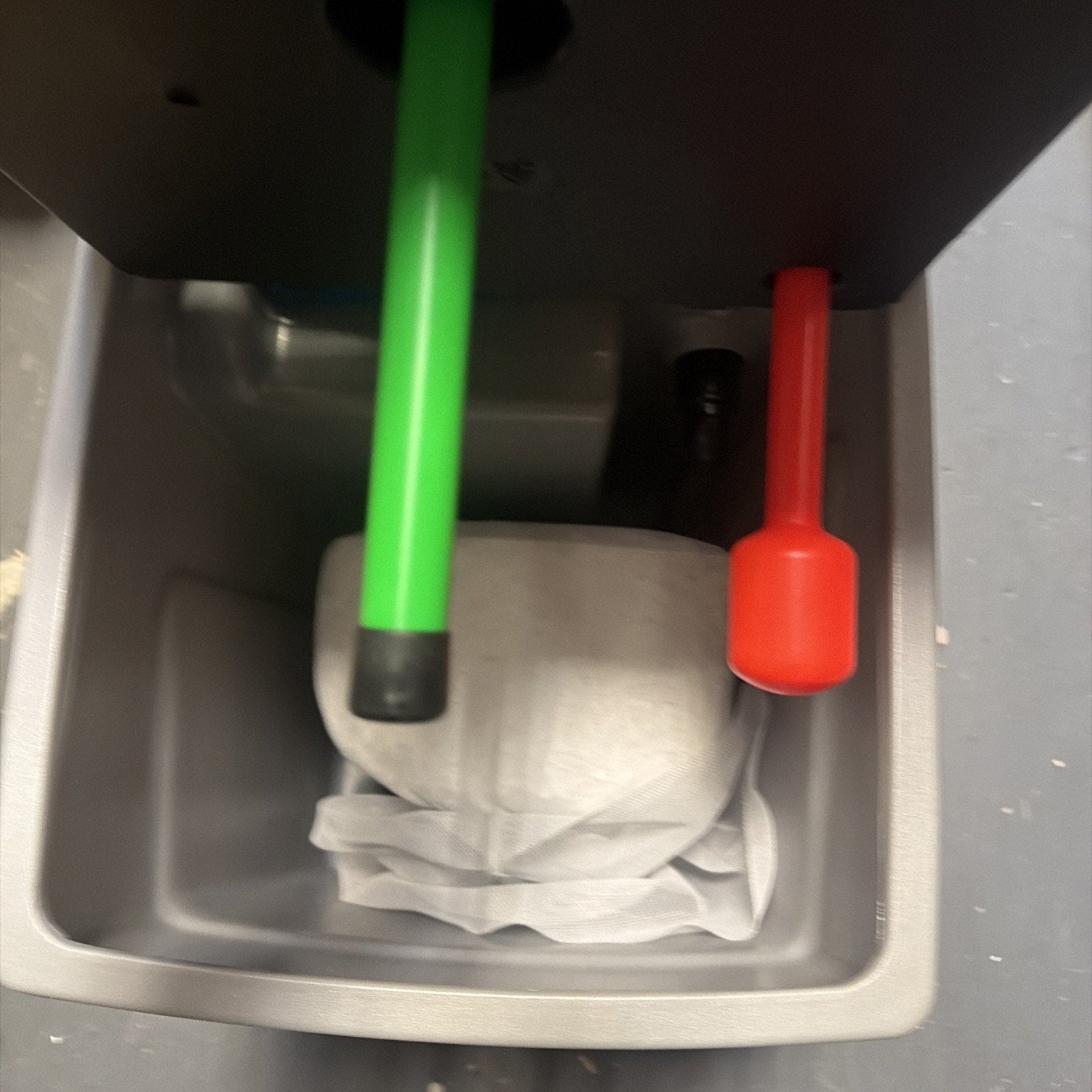 Close-up view of a gray plastic container holding a crumpled white cloth, with two vertically positioned sticks—one green with a black tip and one red with a rounded end—protruding from above.