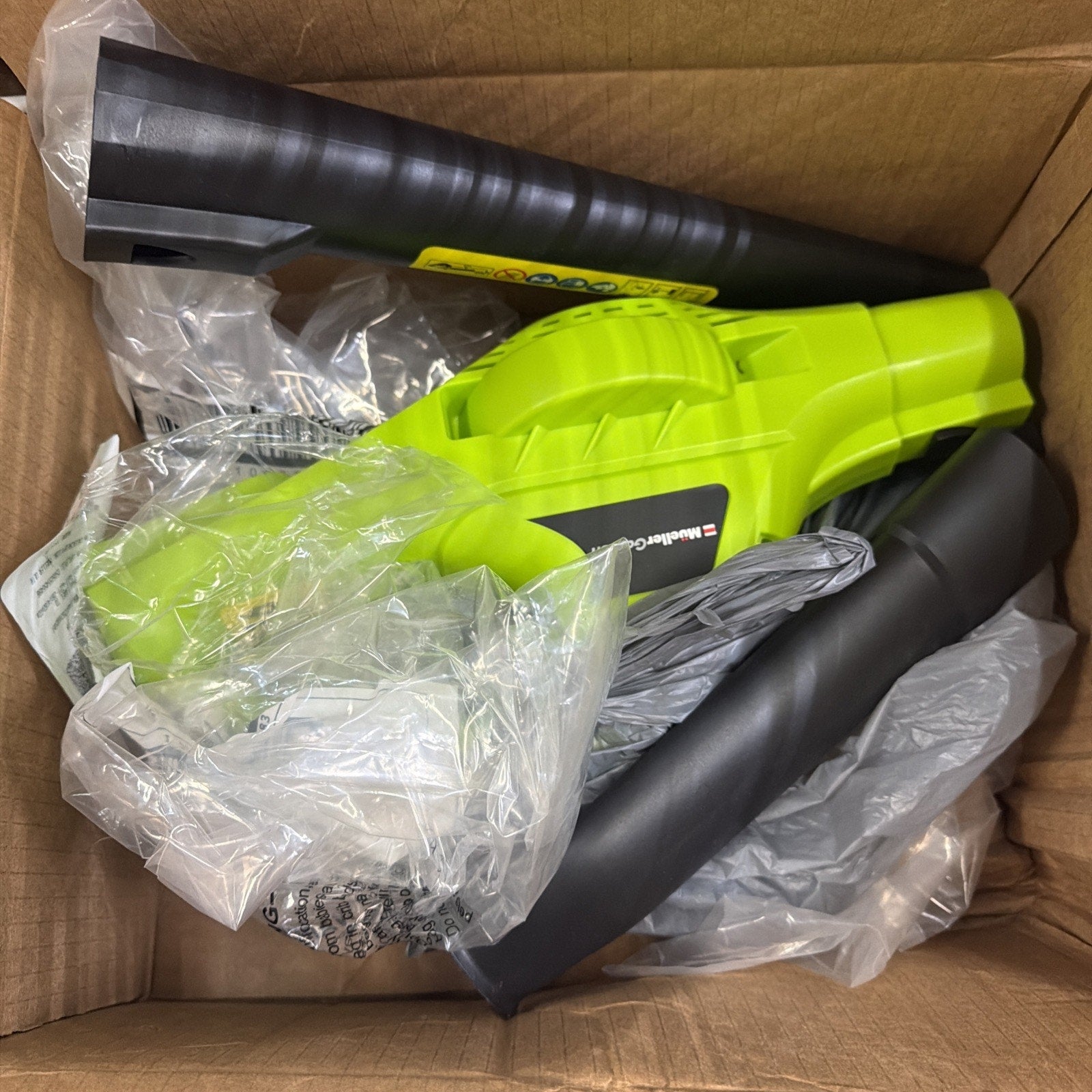Contents of a cardboard box including a bright green handheld leaf blower with black attachments and protective plastic wrapping inside.
