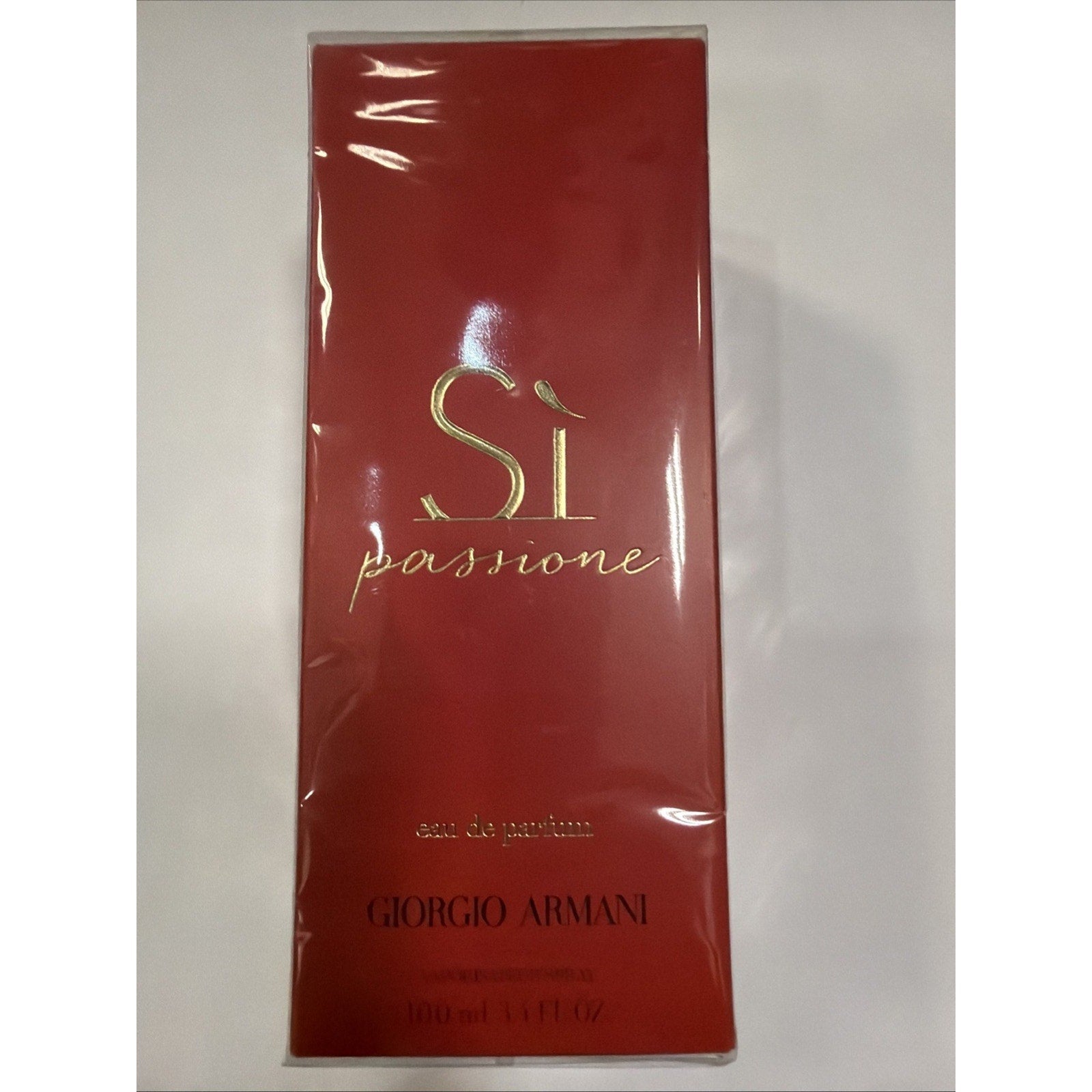 Rectangular bottle packaging in deep red with glossy finish, featuring gold embossed "Sì passione" text and Giorgio Armani branding near the bottom.