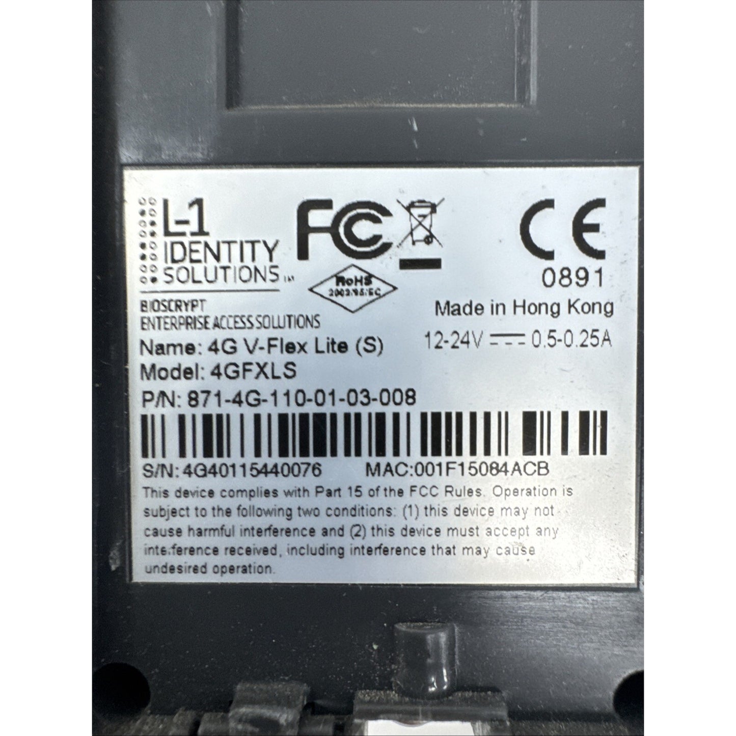 Close-up of a white label on a black electronic device showing certification logos including FCC and CE, model and serial numbers, power specifications, and manufacturing details from Hong Kong.