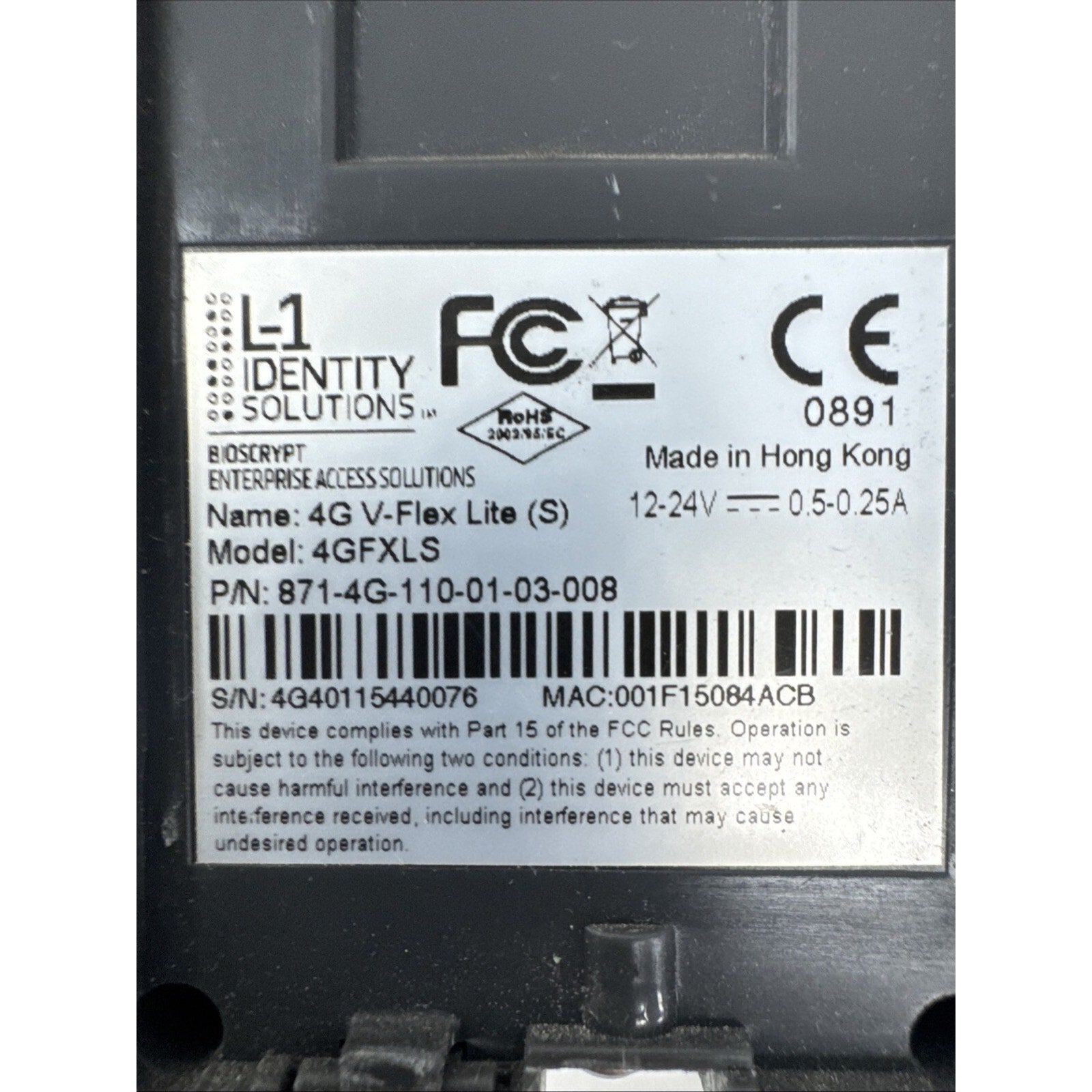 Close-up of a white label on a black electronic device showing certification logos including FCC and CE, model and serial numbers, power specifications, and manufacturing details from Hong Kong.