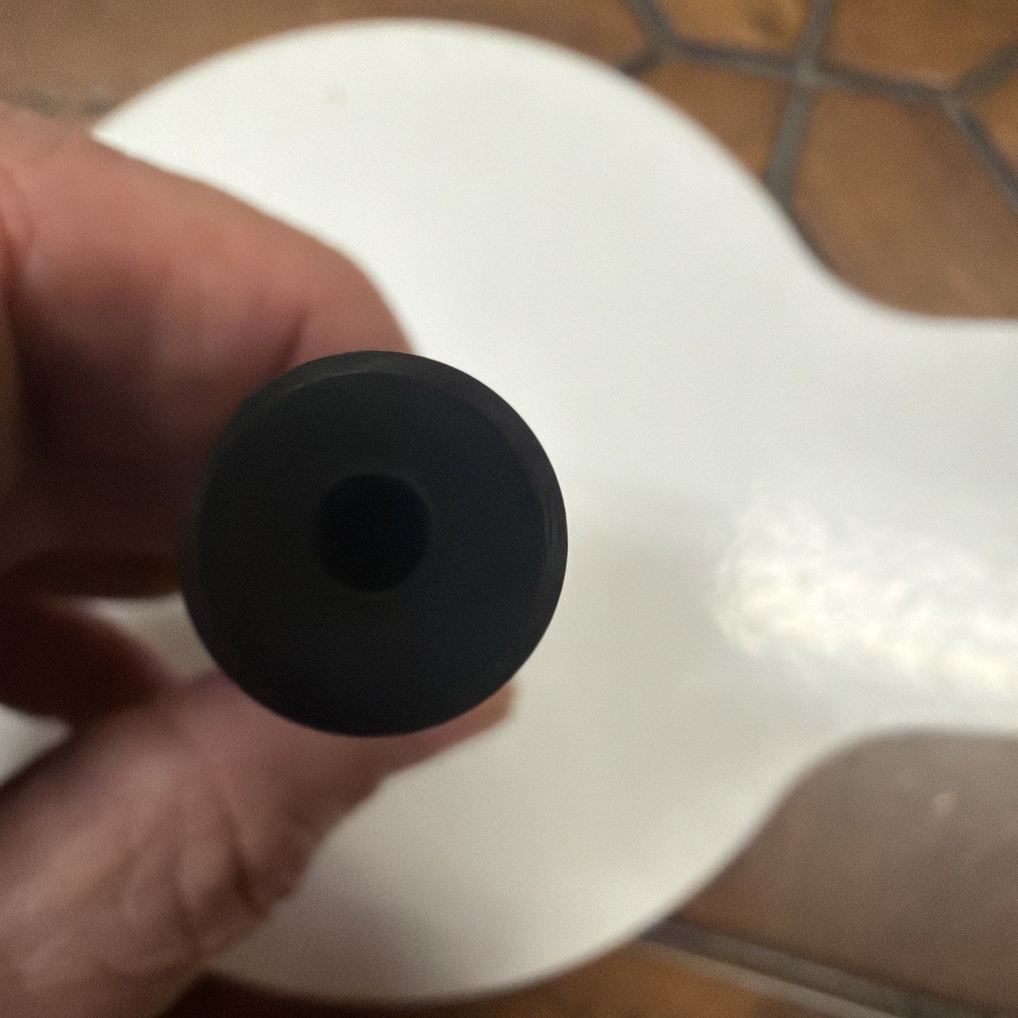 Close-up image of a black cylindrical object with a hollow center held by a hand, against a white and brown tiled background.