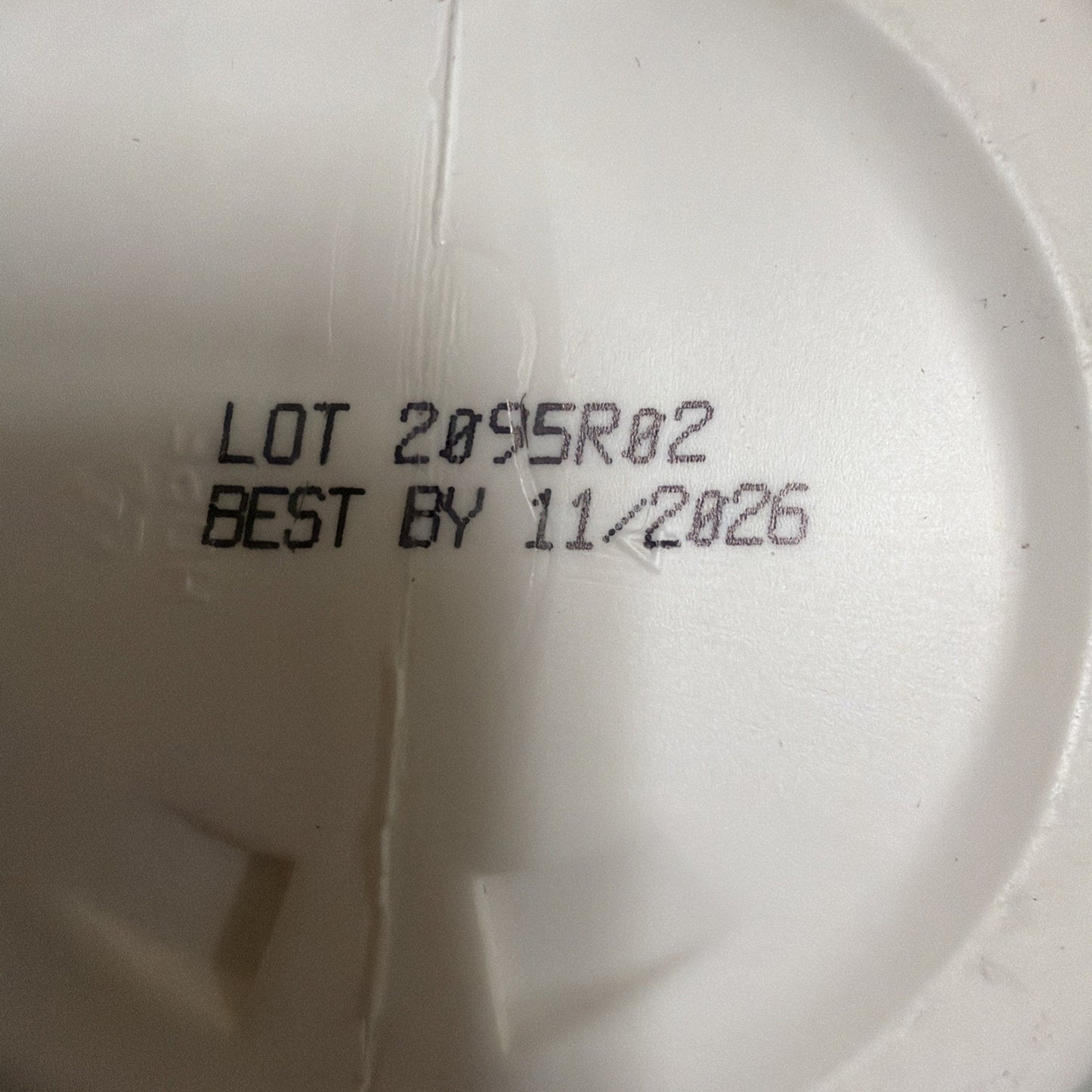 Close-up of black printed lot number 2095R02 and best by date 11/2026 on a white textured plastic surface.