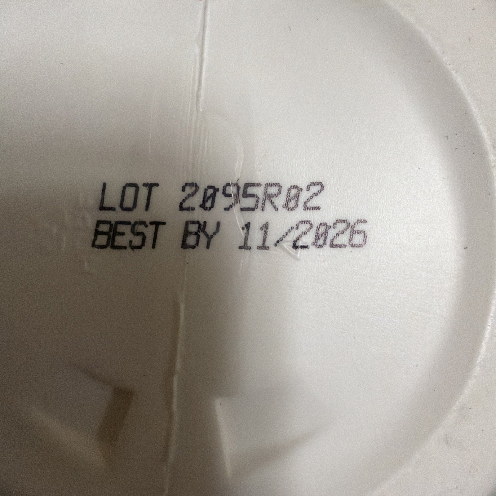 Close-up of black printed lot number 2095R02 and best by date 11/2026 on a white textured plastic surface.