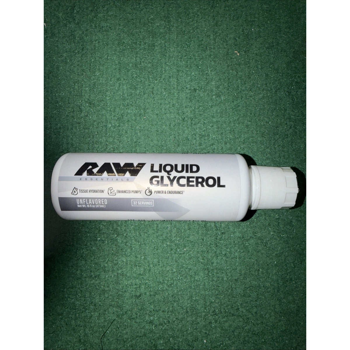 White cylindrical bottle labeled "RAW Liquid Glycerol" with unflavored text and icons indicating tissue hydration, enhanced pumps, and power endurance, lying horizontally on a green textured surface.