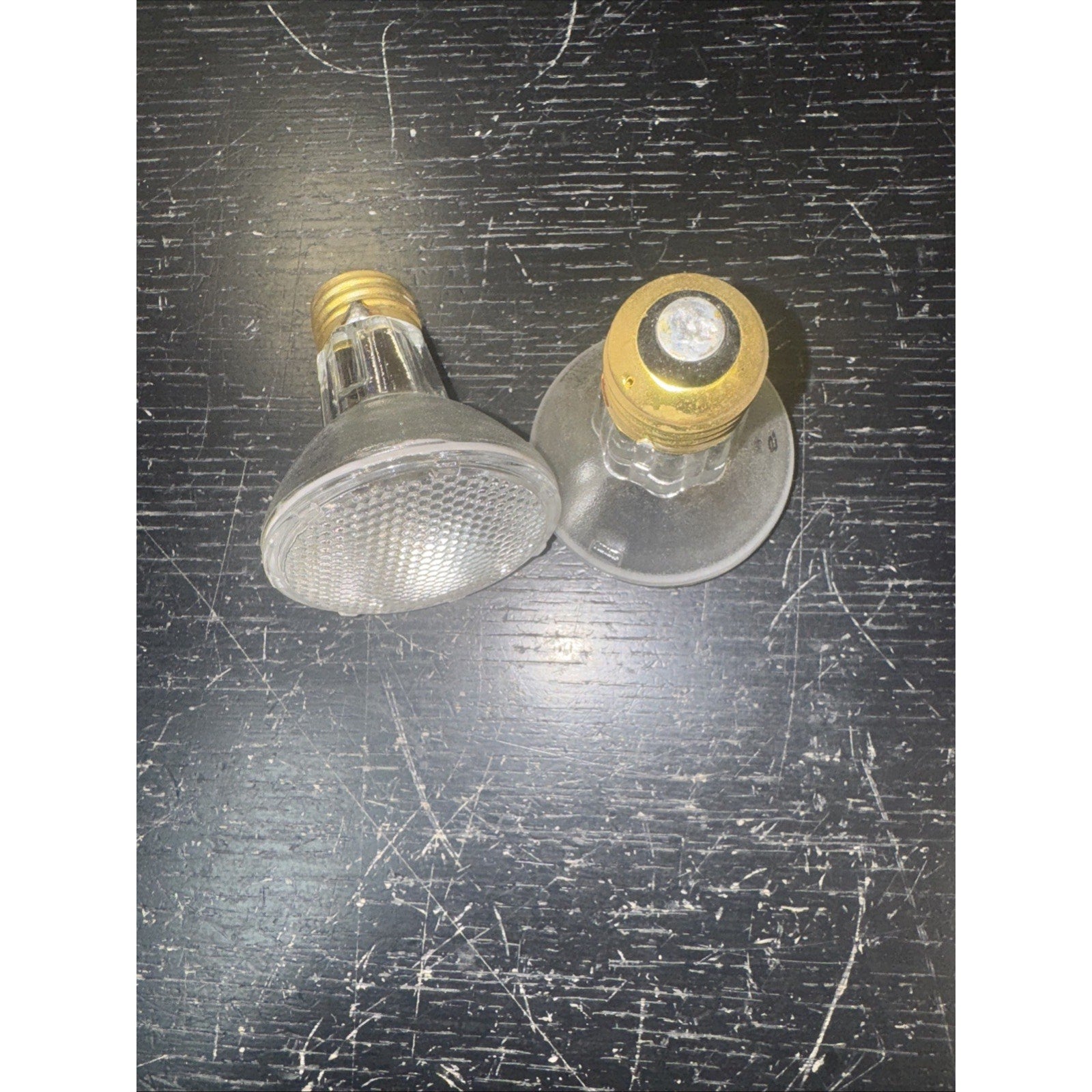 Two replacement 50PAR20/H/FL 120V 50W bulbs with brass screw bases on scratched dark surface