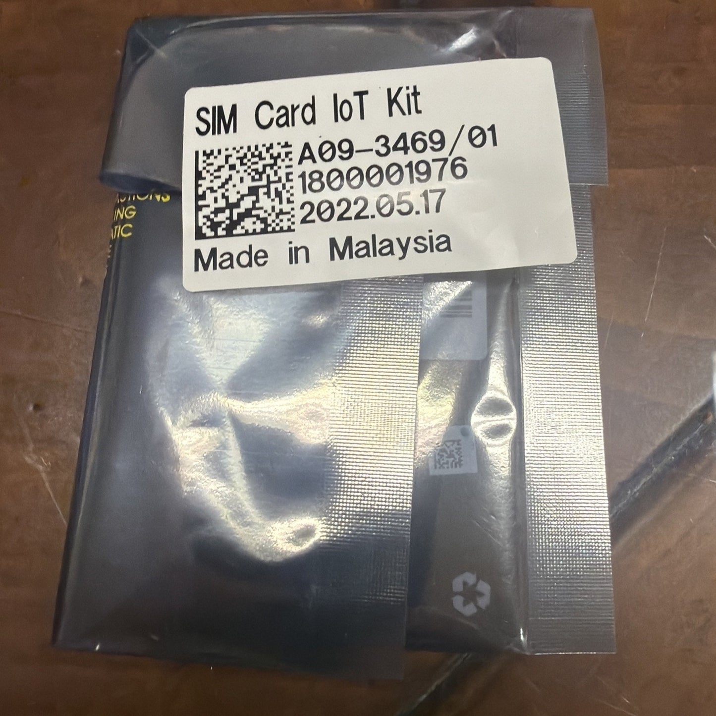 Sealed gray anti-static plastic package containing a SIM Card IoT Kit with a white label showing product code, batch number, manufacturing date, and "Made in Malaysia" text.