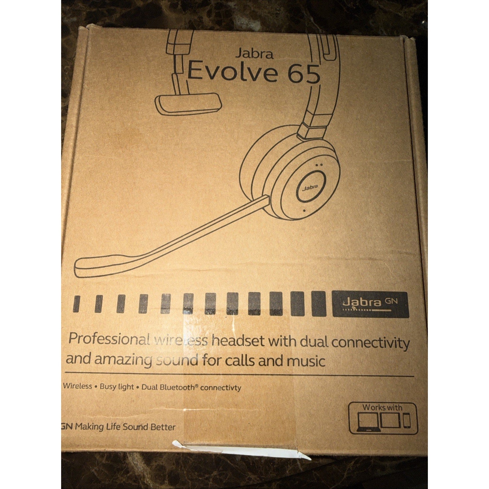 Brown cardboard box showing a simple line drawing of a Jabra Evolve 65 wireless headset, highlighting dual Bluetooth connectivity and features for calls and music.