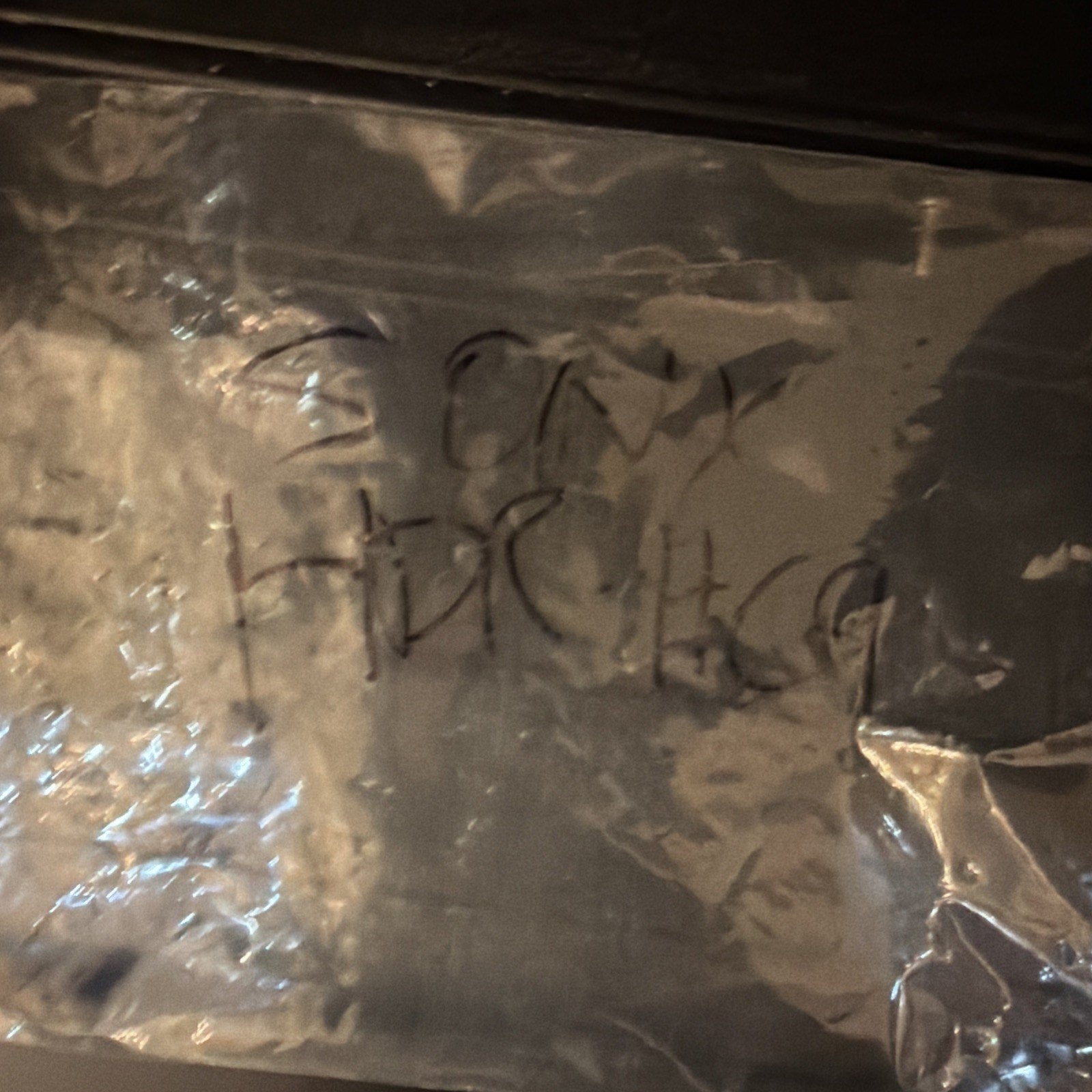 Close-up of a crinkled, transparent plastic bag with faint black handwritten text visible through the material, under warm lighting.