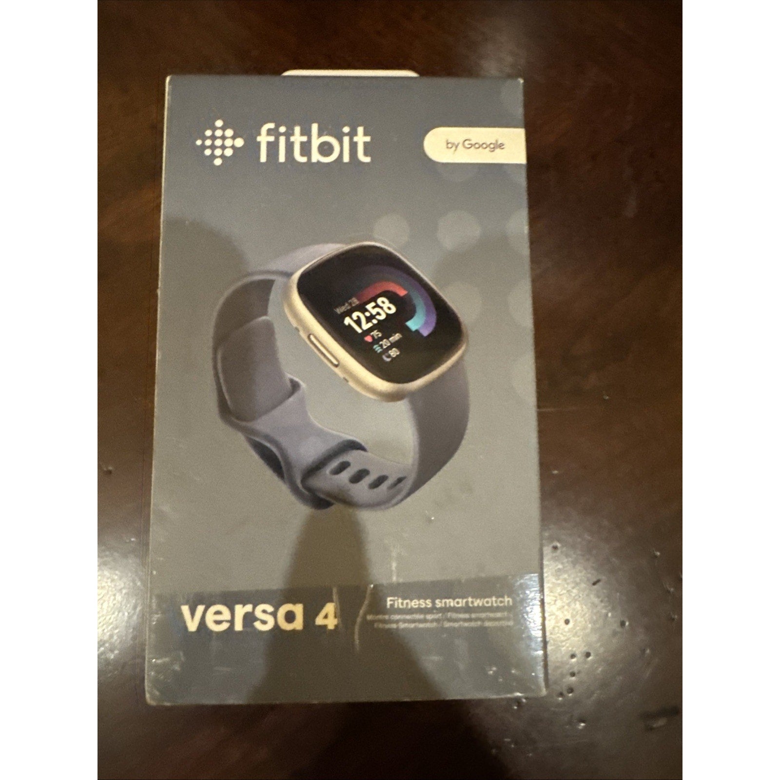Fitbit Versa 4 fitness smartwatch in Waterfall Blue with Platinum Aluminum Case on retail packaging box front view