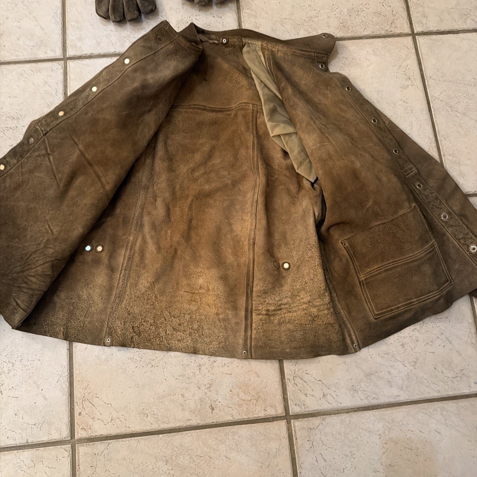 Heavy-duty leather welding jacket coat open flat on tile floor showing interior lining and pocket details