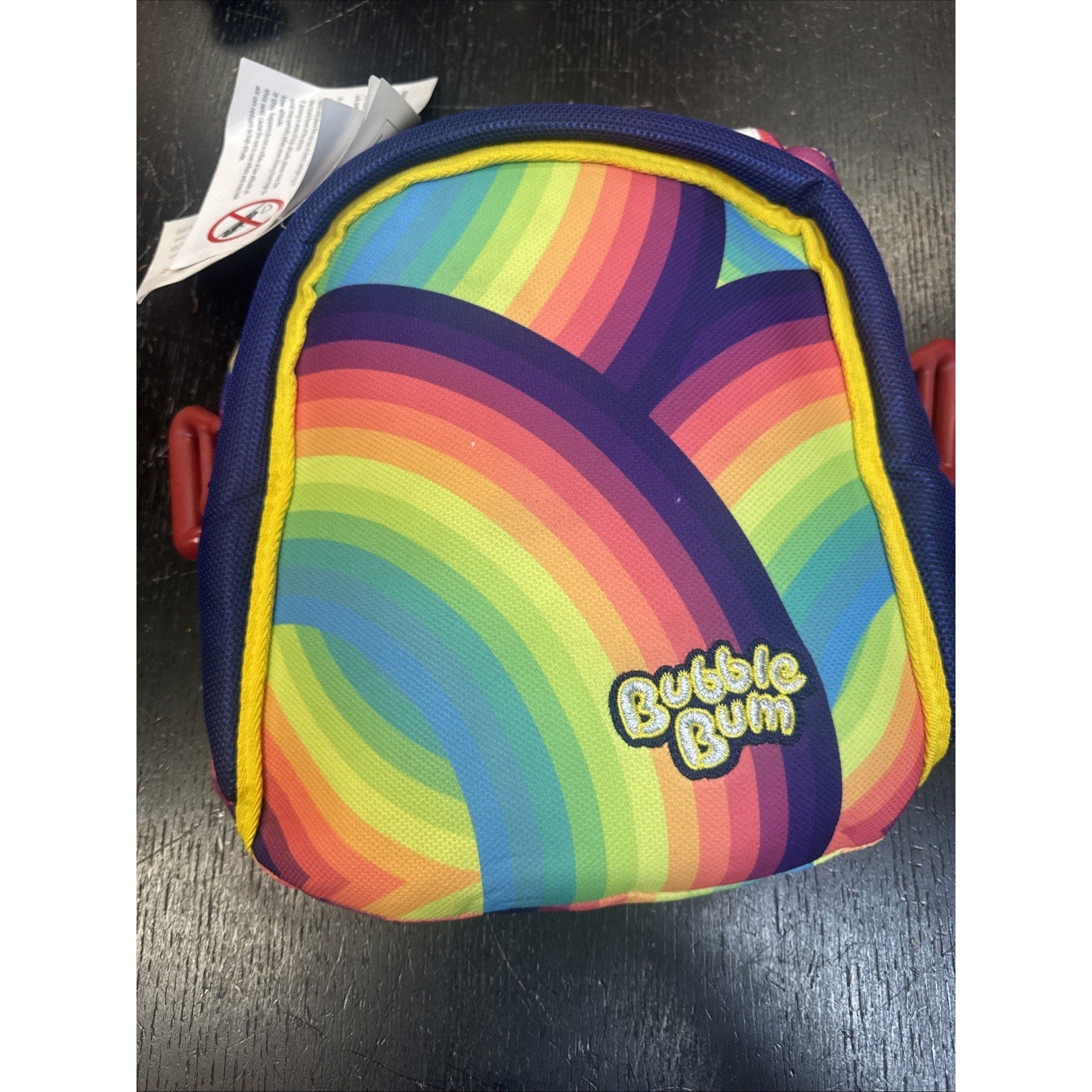Compact Bubble Bum inflatable backless booster car seat folded with rainbow pattern and logo on black surface
