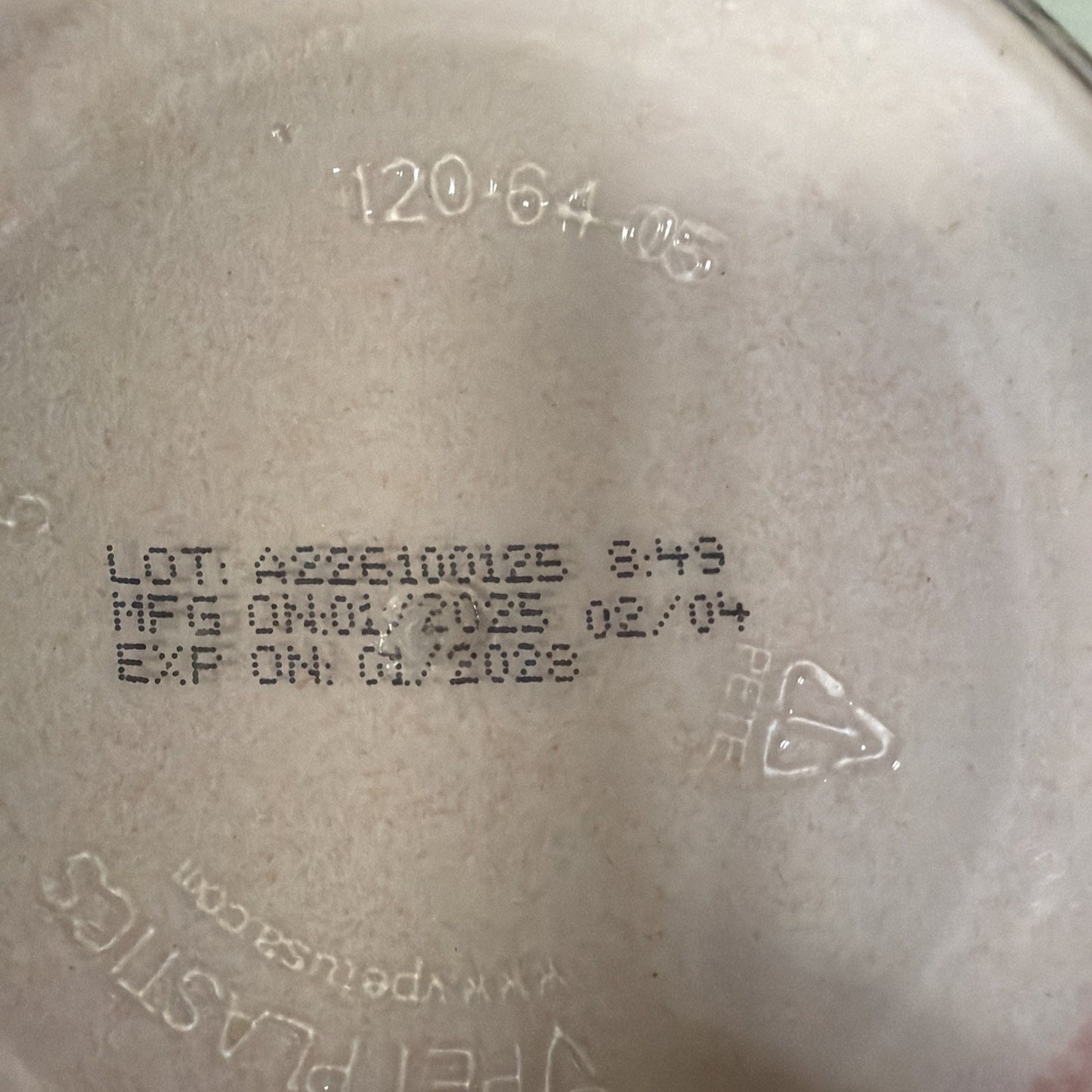 Close-up of a beige plastic surface showing batch number AZ26100123, manufacturing date 02/04, expiration date 01/2028, recycling symbol with PETE code, and faint embossed text.
