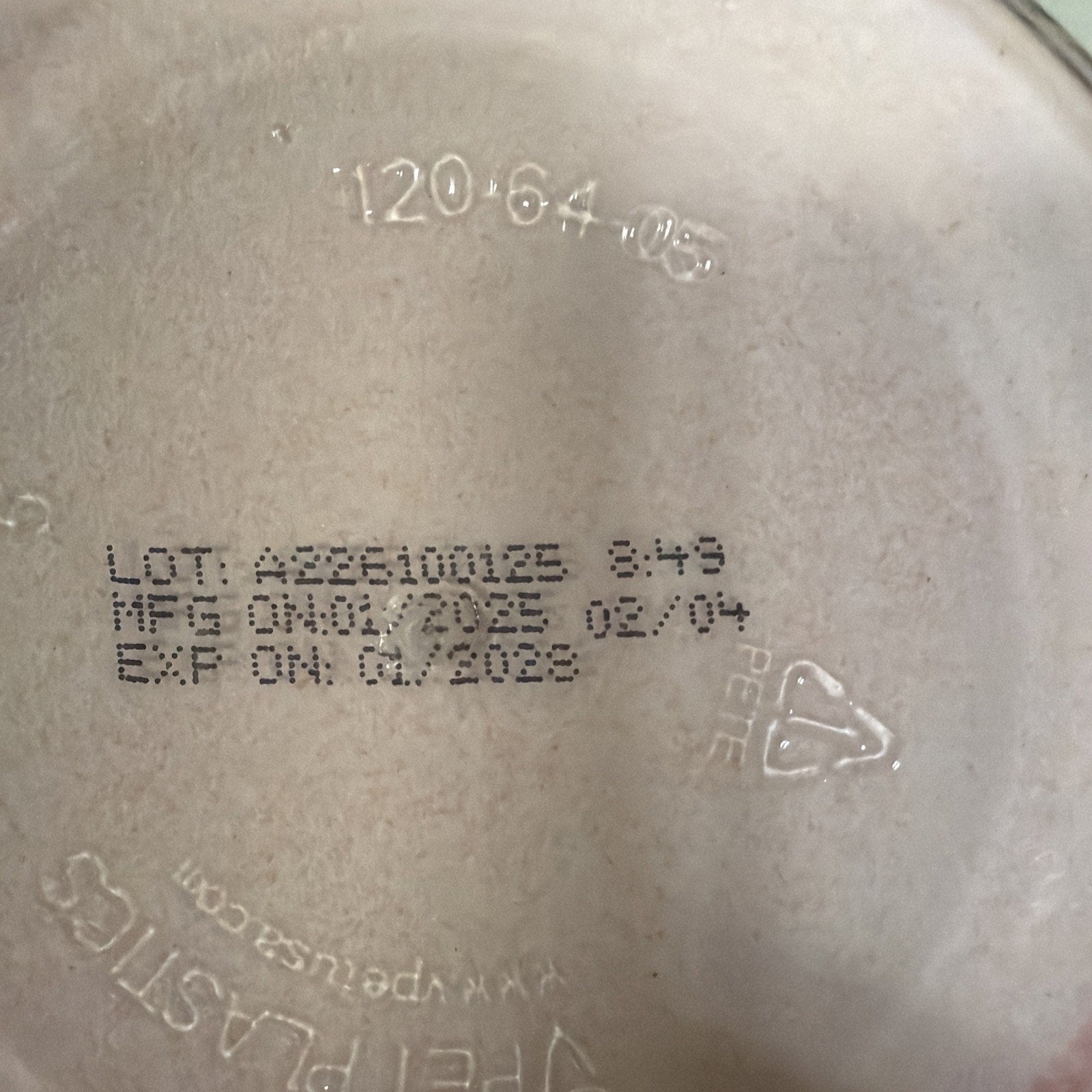 Close-up of a beige plastic surface showing batch number AZ26100123, manufacturing date 02/04, expiration date 01/2028, recycling symbol with PETE code, and faint embossed text.