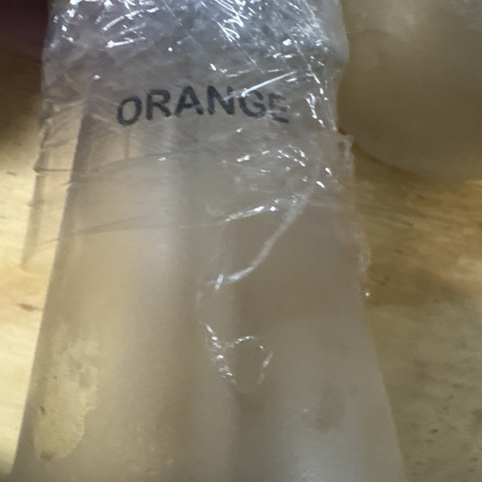 Close-up of oxygen bar scent bottle labeled Orange wrapped in clear plastic on wooden surface