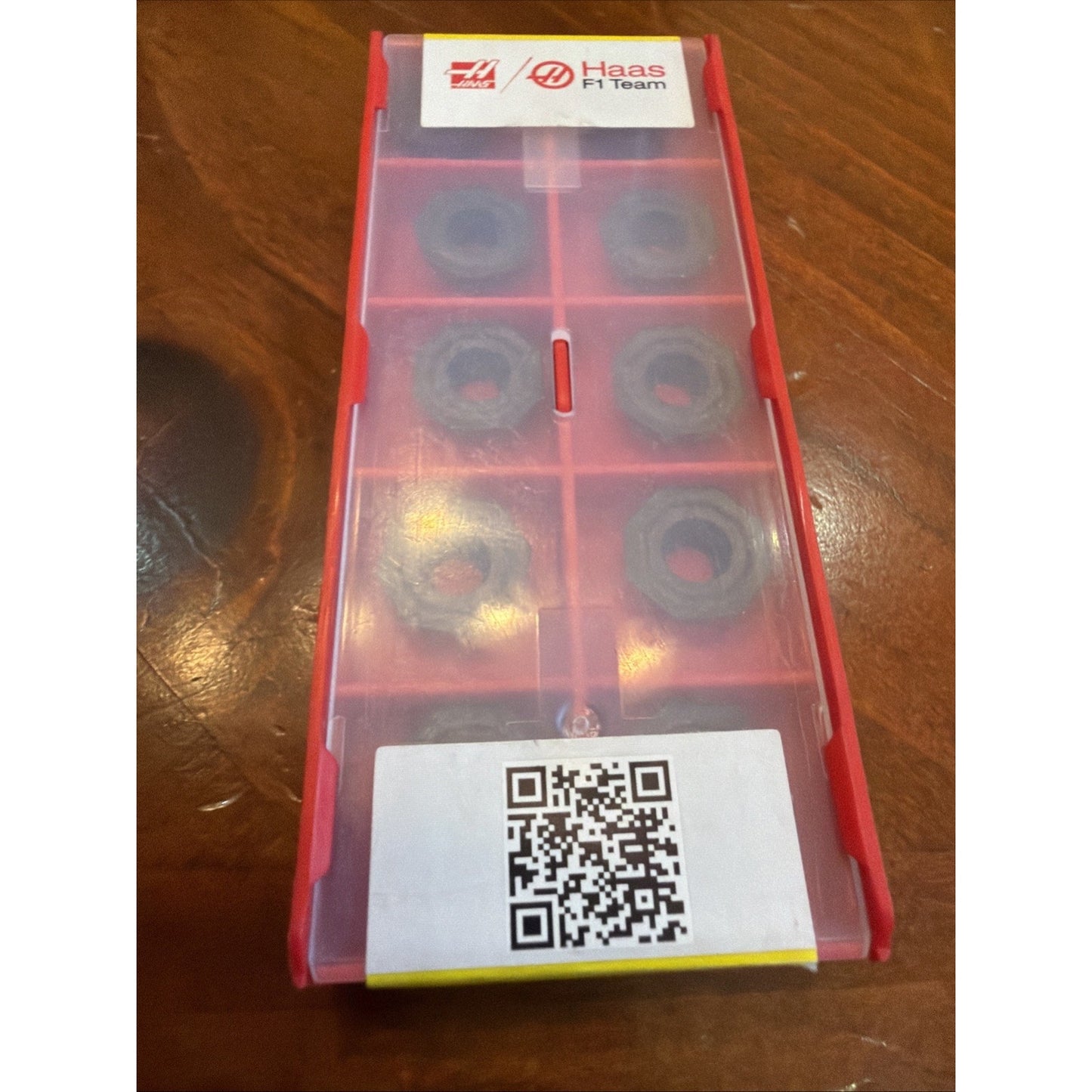 Red plastic storage box with a translucent lid containing eight round metal inserts arranged in individual compartments, featuring Haas F1 Team branding and a QR code label.
