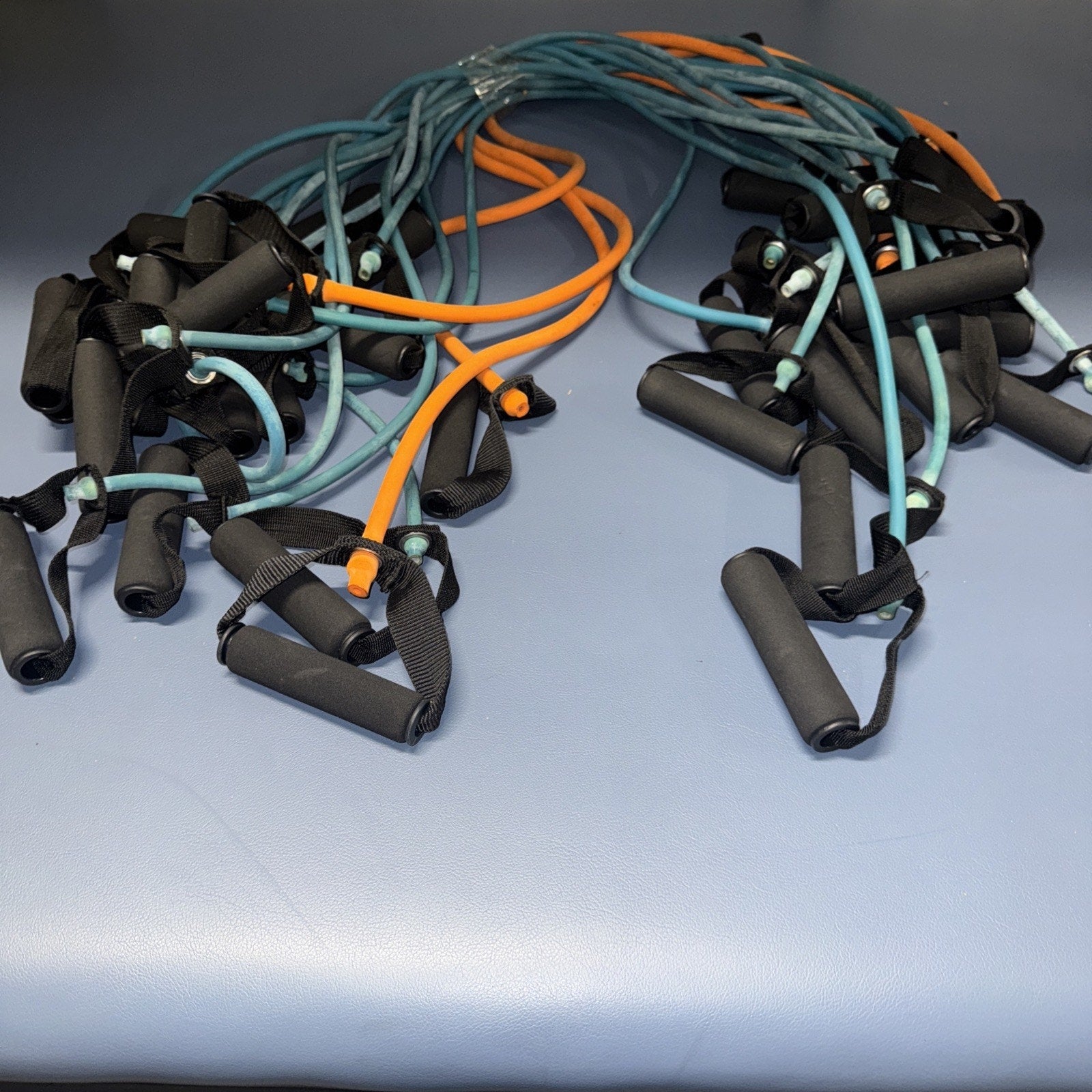 Set of 18 multicolor fitness resistance bands with black foam handles arranged on blue surface for home workouts