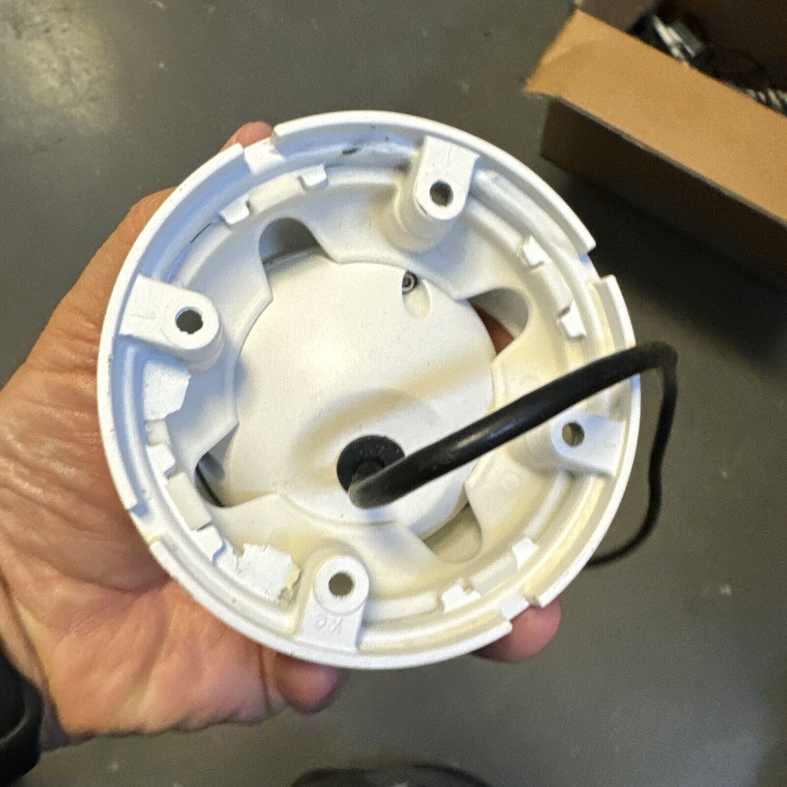 Bottom view of white analog CCTV dome camera housing showing mounting points and attached black cable