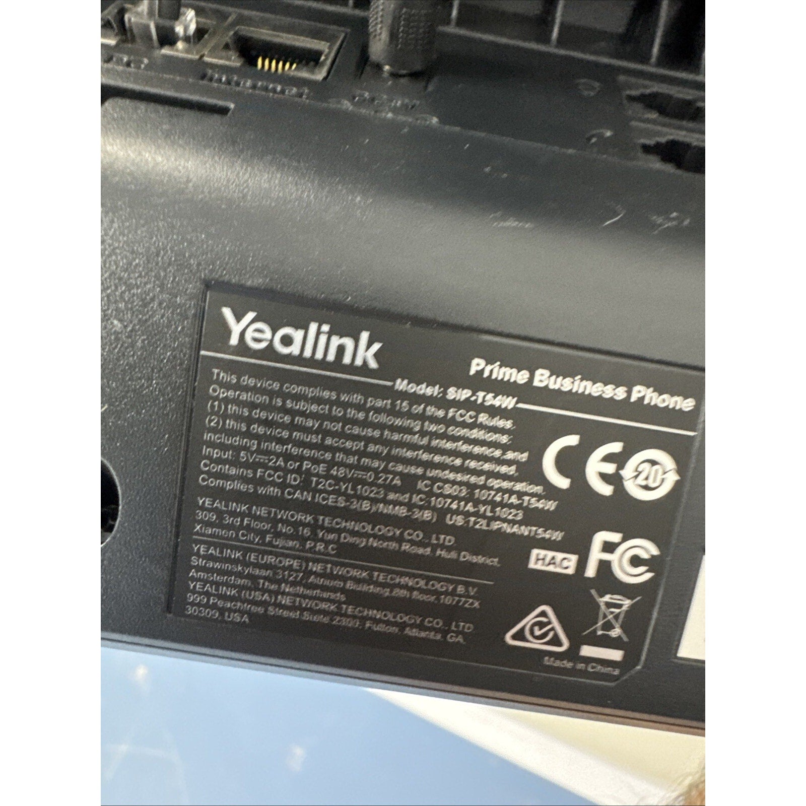Close-up of a black Yealink Prime Business Phone showing regulatory labels, model number SIP-T54W, certification marks including FCC and CE, and manufacturing information.