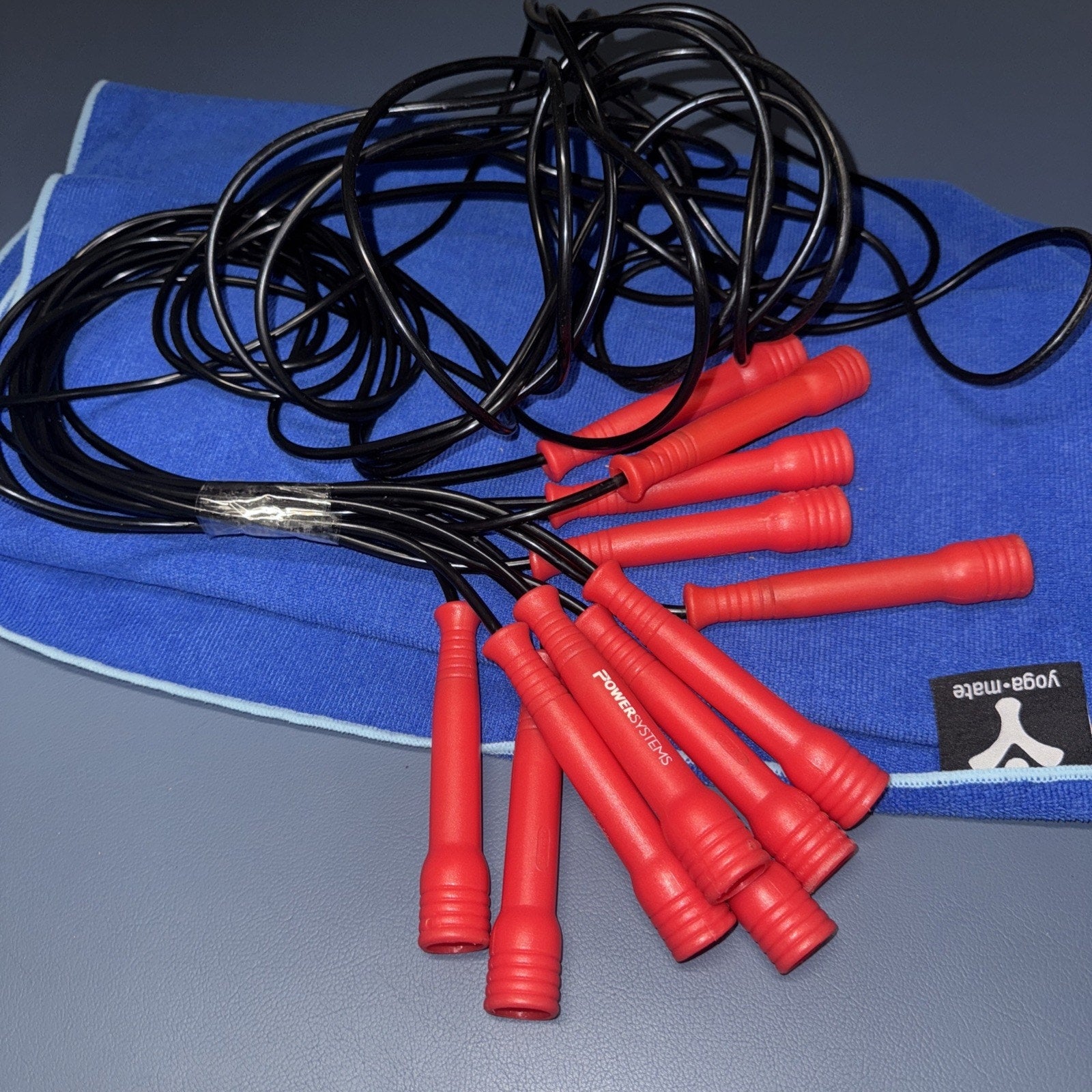 6 Power Systems jump ropes with red handles and black cords laid on blue Yoga-Mat workout mat