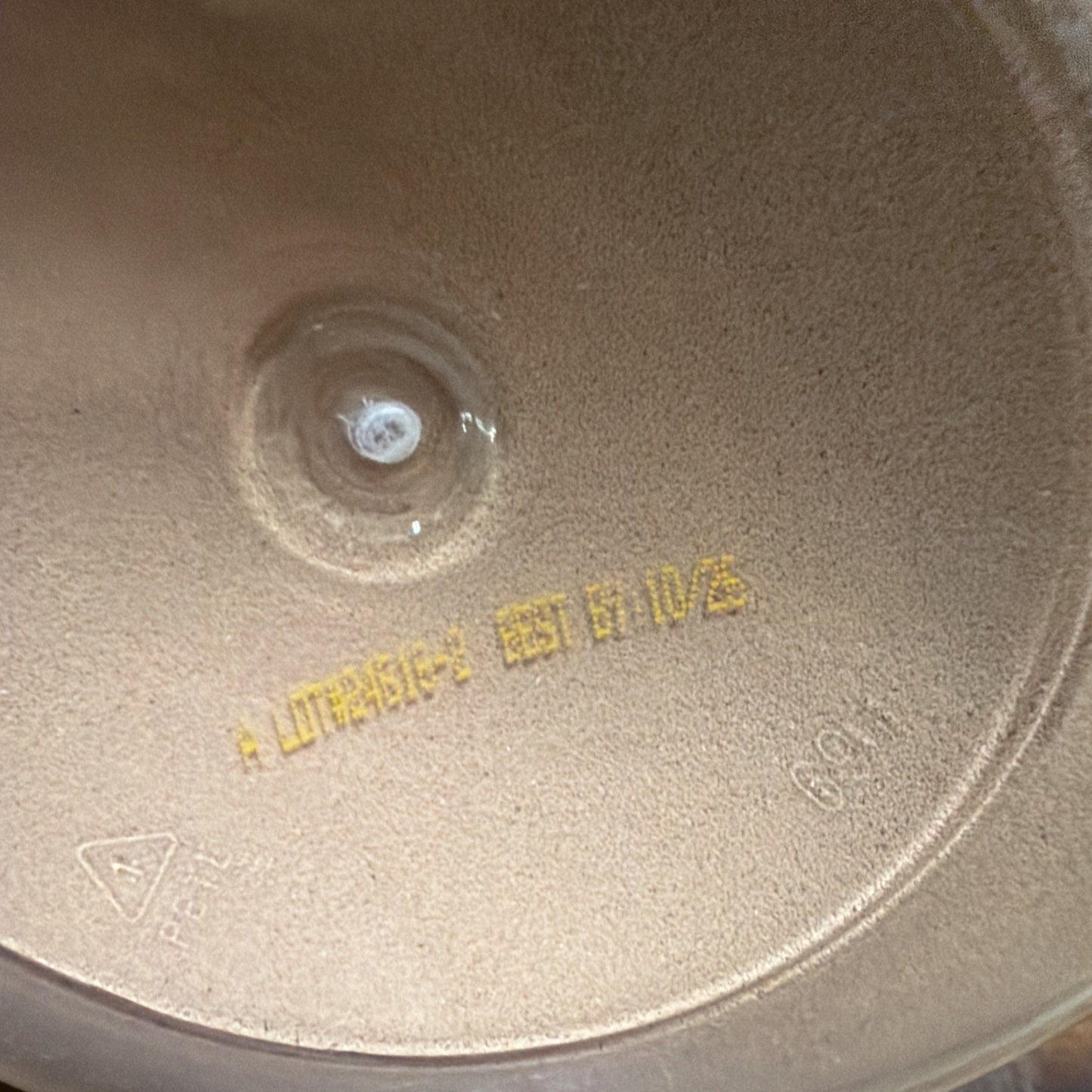 Close-up of a powdery beige surface inside a container, featuring a pressed circular indentation and stamped yellow text indicating a lot number and best-by date.
