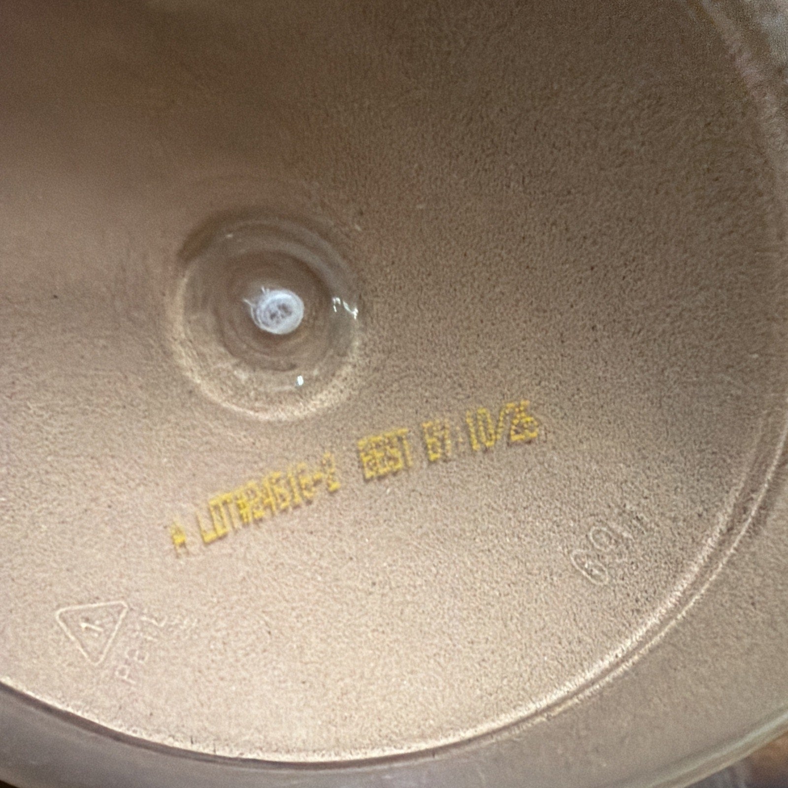 Close-up of a powdery beige surface inside a container, featuring a pressed circular indentation and stamped yellow text indicating a lot number and best-by date.