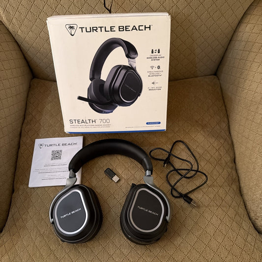Turtle Beach Stealth 700 Gen 3 wireless gaming headset in black with box, USB dongle, charging cable, and manual on couch