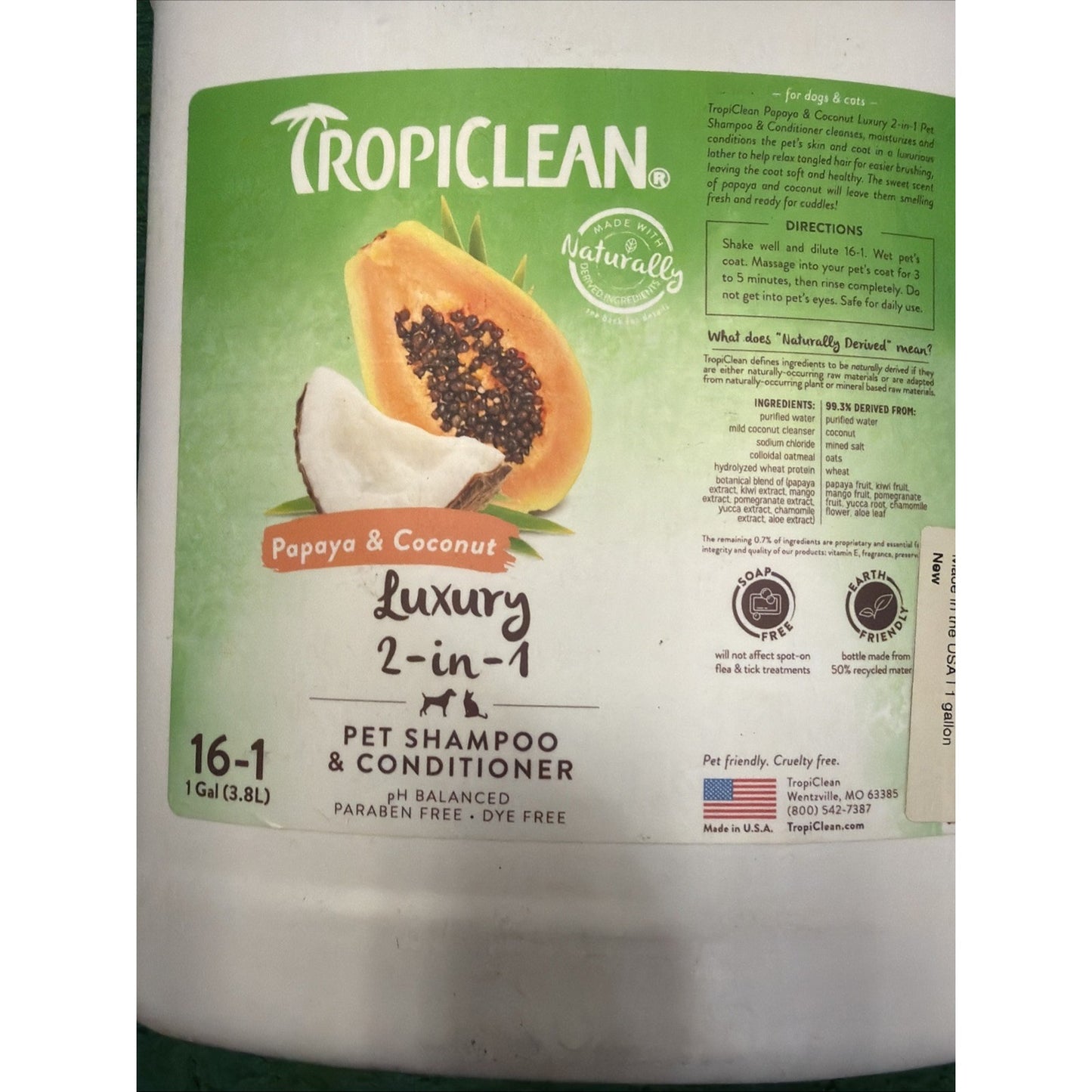 Close-up of a white plastic gallon container with a green label featuring images of papaya and coconut, indicating luxury 2-in-1 pet shampoo and conditioner with natural ingredients.