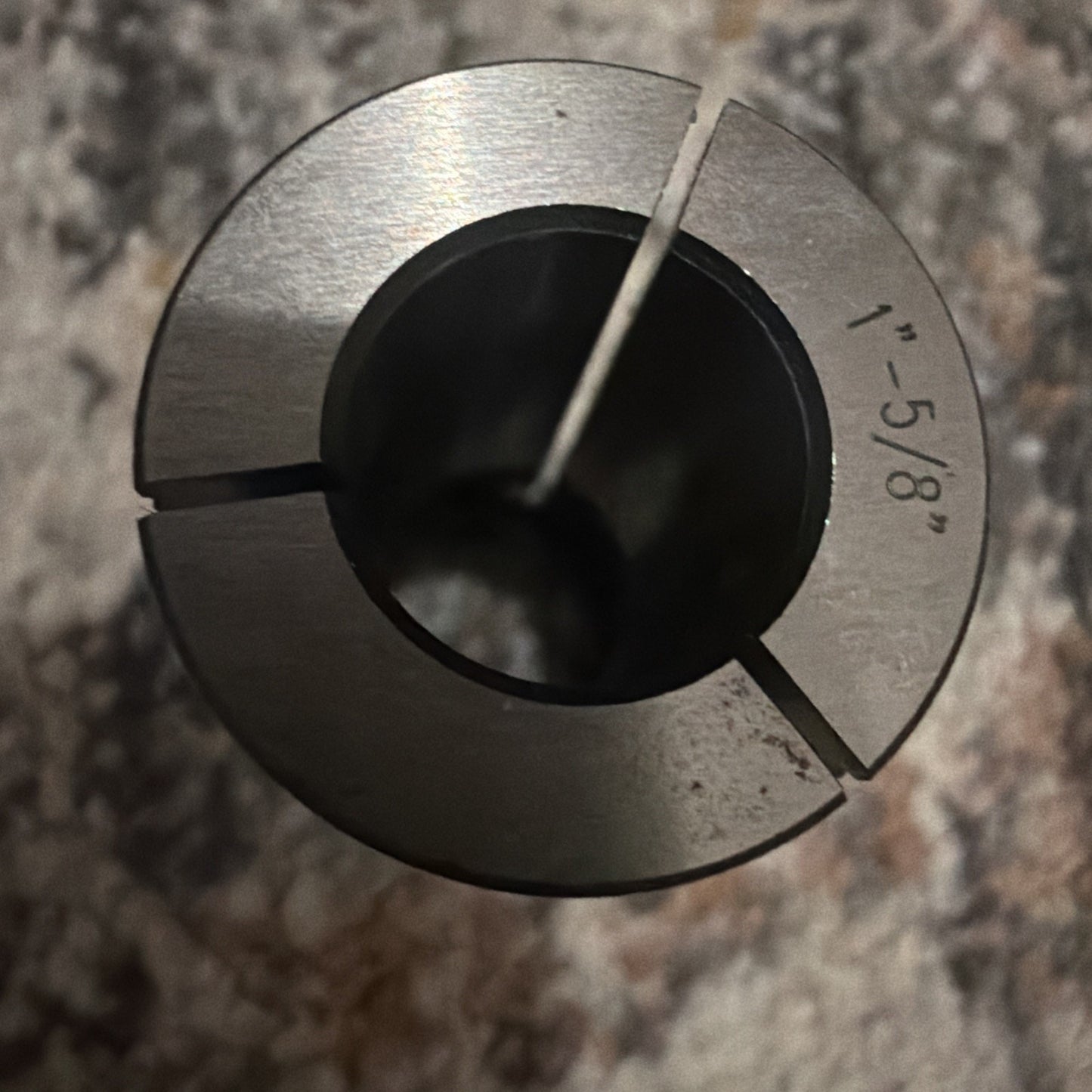 Top view of a metallic cylindrical collet with three evenly spaced slits and engraved measurement marking 1"-5/8", placed on a textured surface.