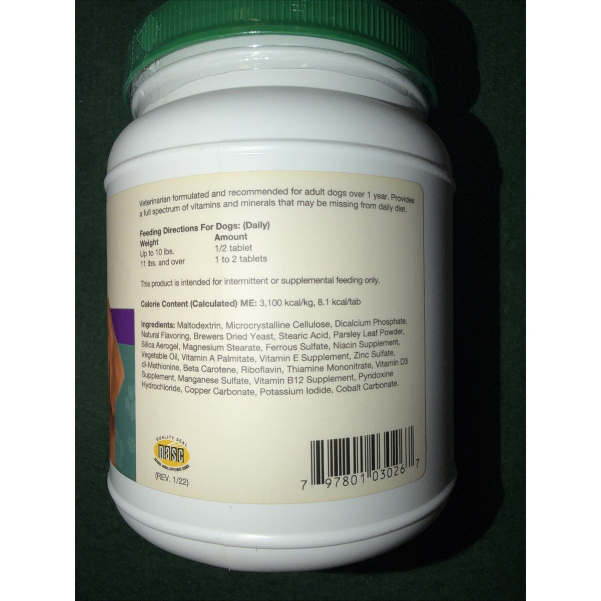 White plastic supplement container with a green lid showing detailed feeding directions, ingredients list, calorie content, and a barcode on the label against a dark background.