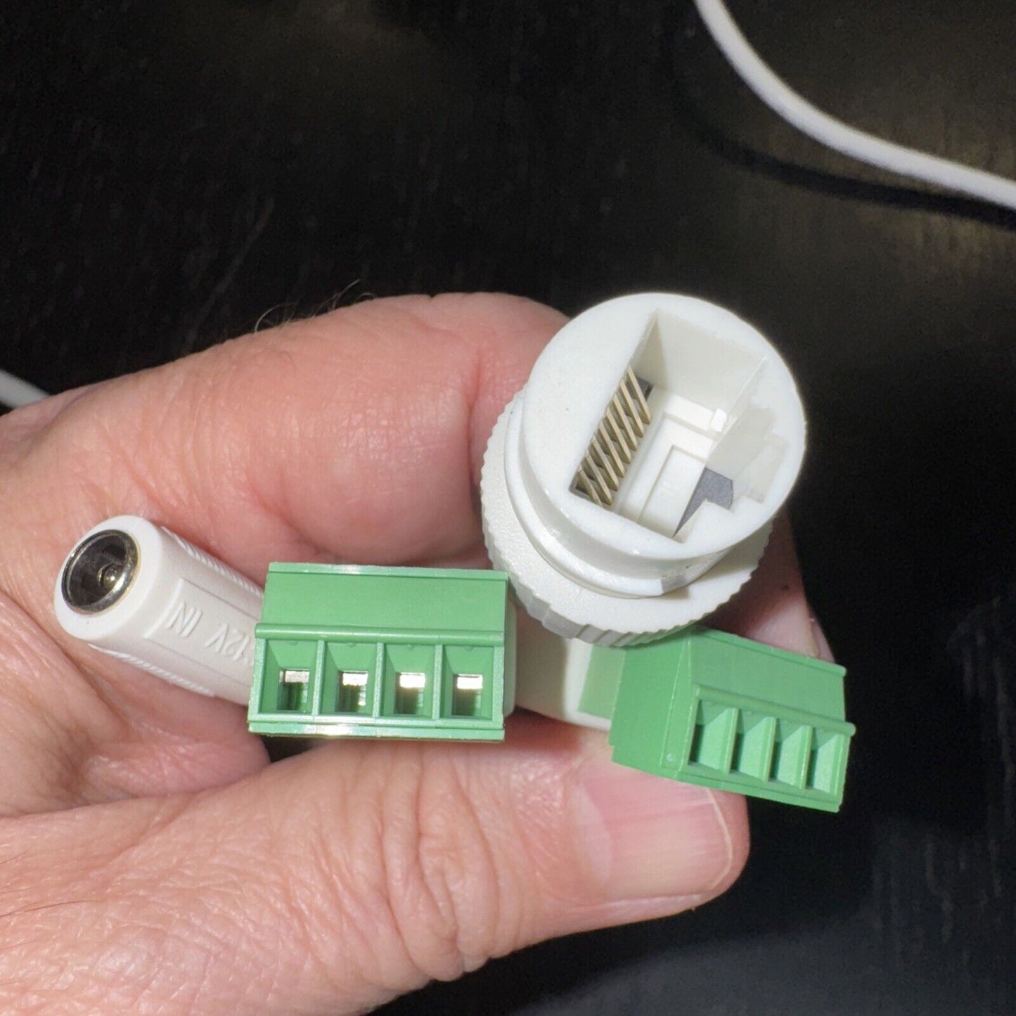 Close-up of hand holding white network camera connectors including RJ45 port and green terminal blocks on black background