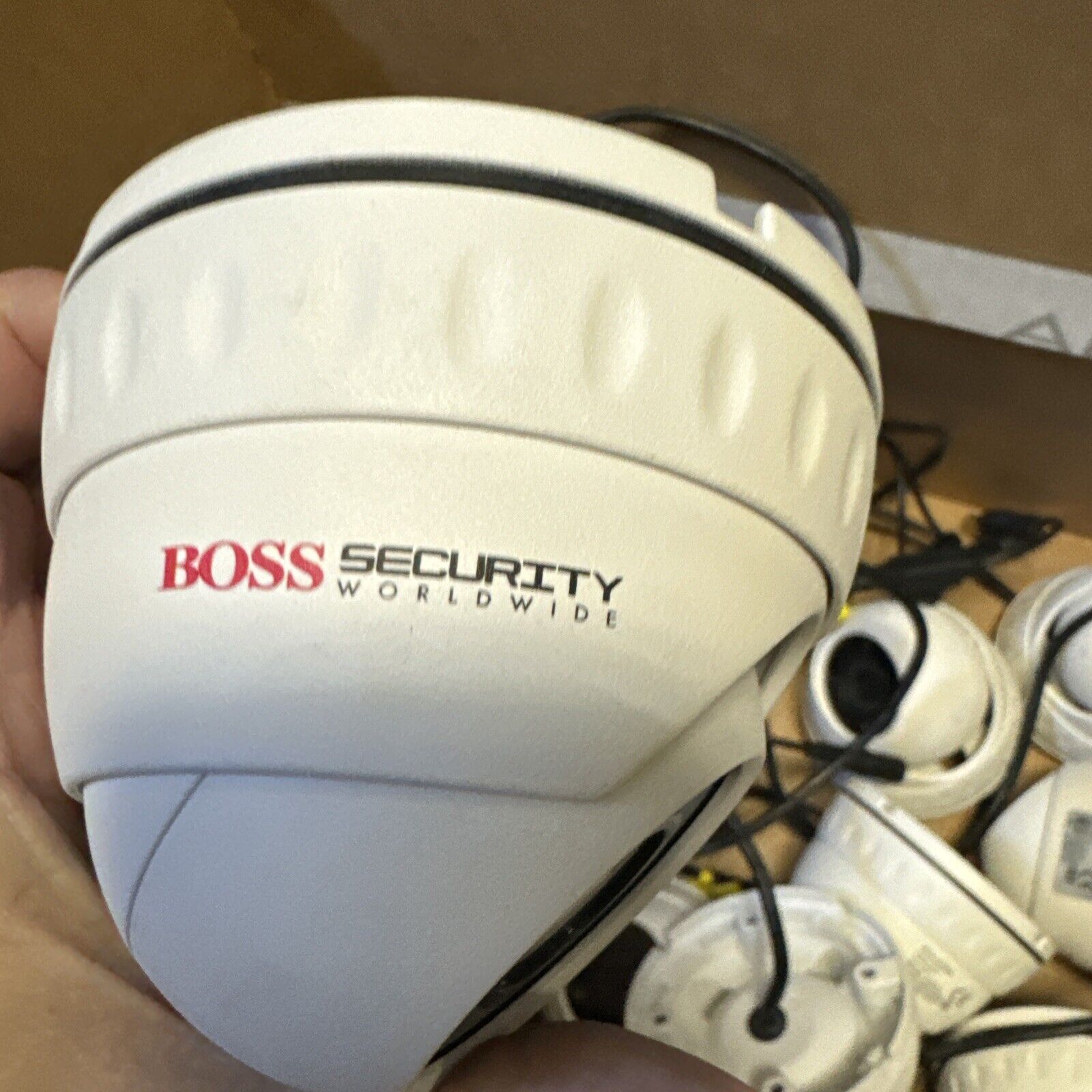 Boss Security Worldwide U9W-1080P white dome surveillance camera held in hand with multiple cameras in background