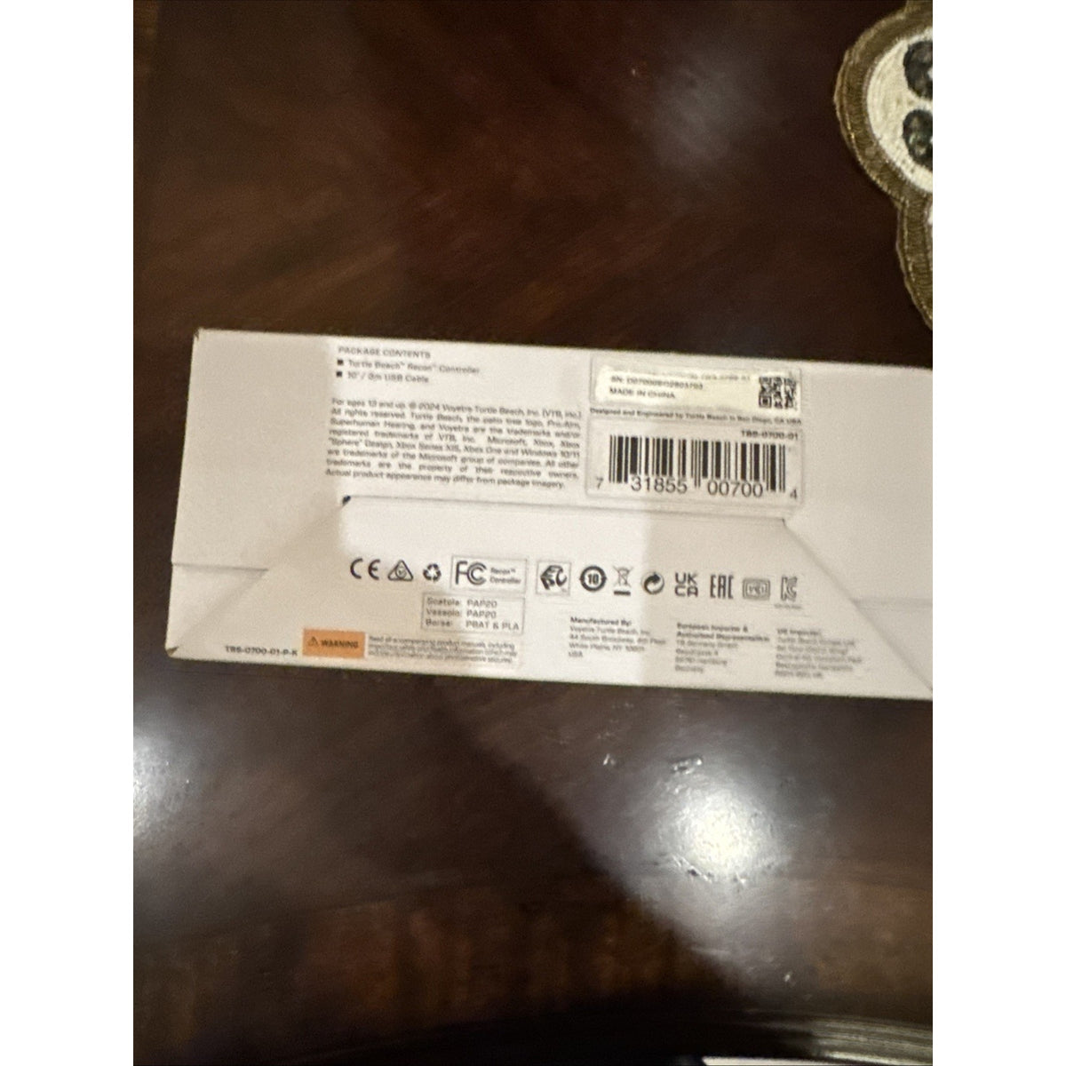 Back of Turtle Beach Recon Controller box showing product details, barcode, and certification symbols on wooden surface