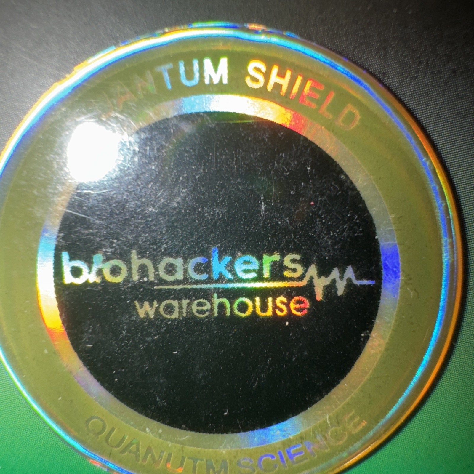 Quantum Shield radiation protection sticker with holographic ring and biohackers warehouse branding on black center background