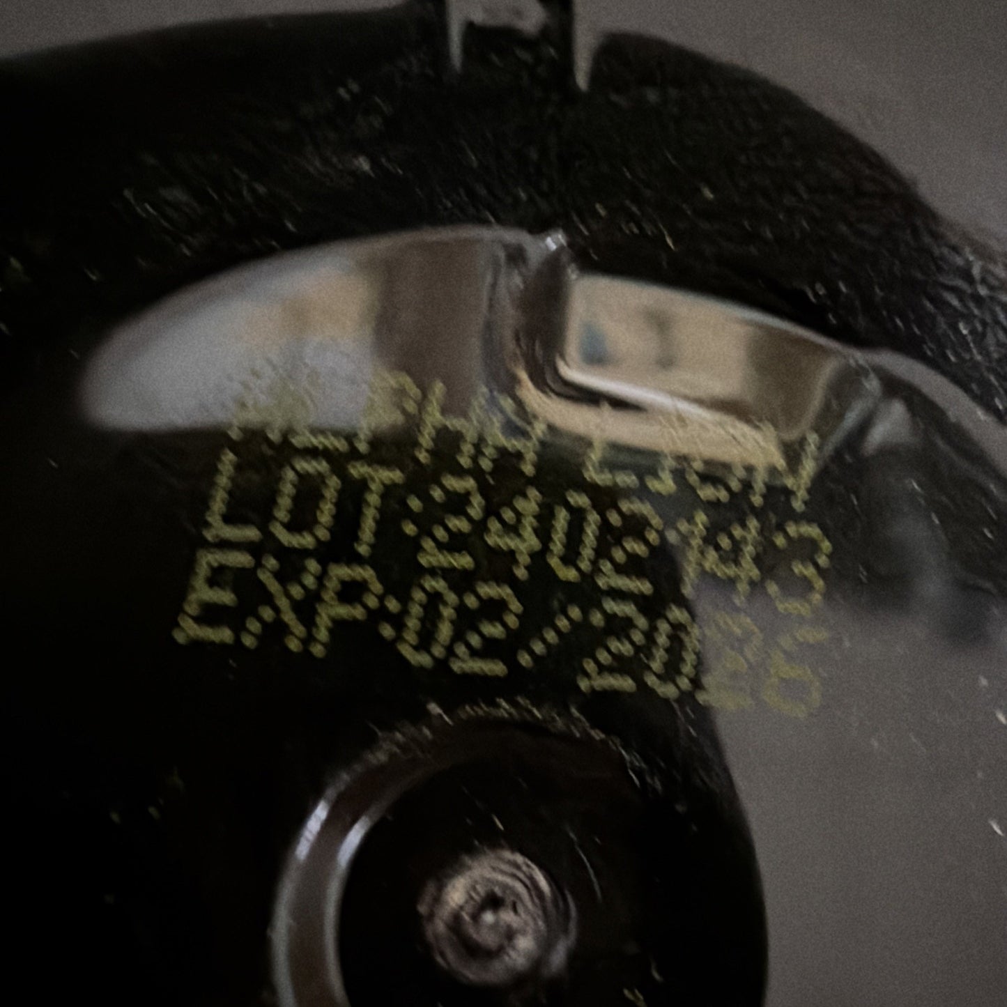 Close-up of a black textured surface with yellow printed lot number "3402143" and expiration date "02/2026" on a metallic reflective area.